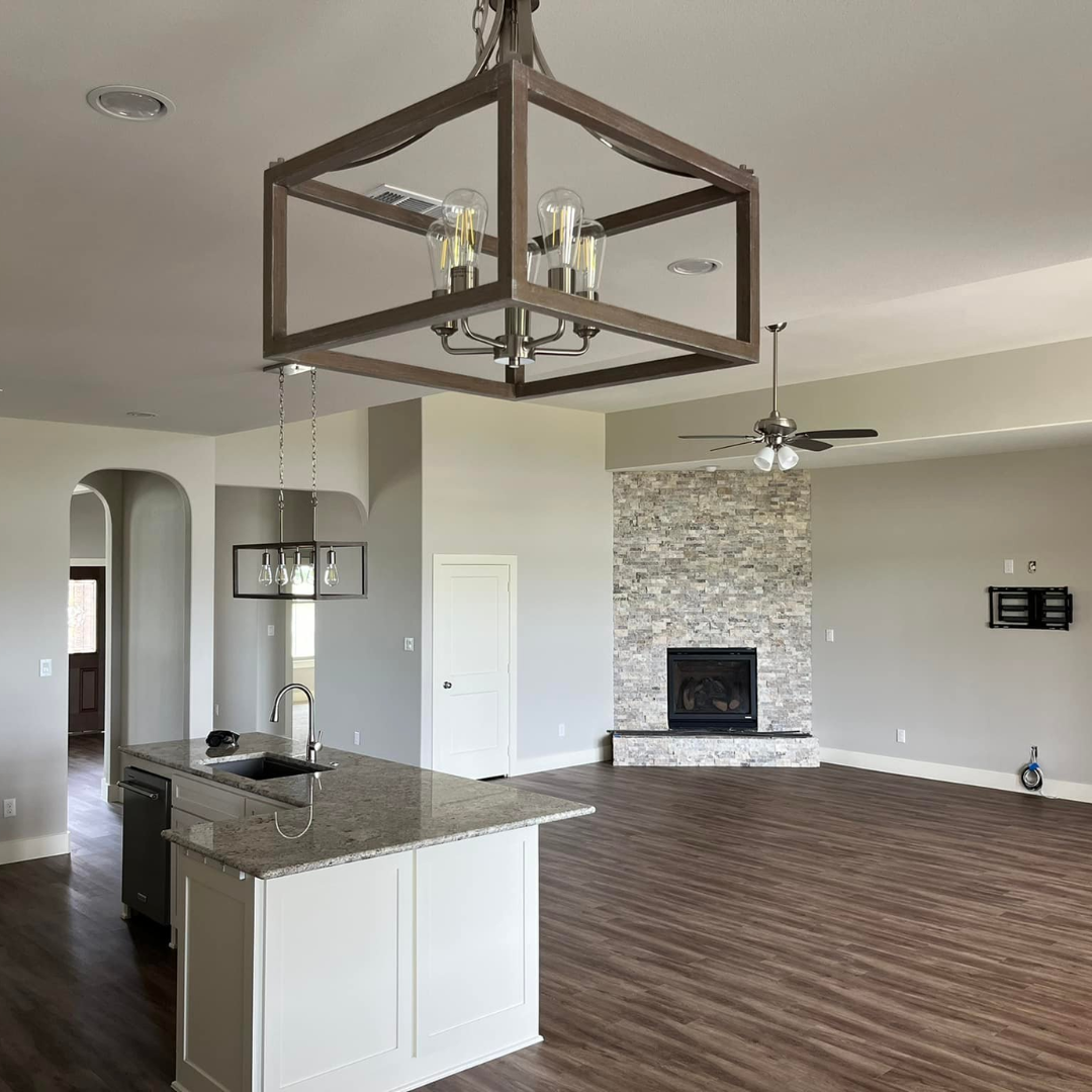 Open-concept living room and kitchen with a stone fireplace, ceiling fan, and modern lighting fixtures.