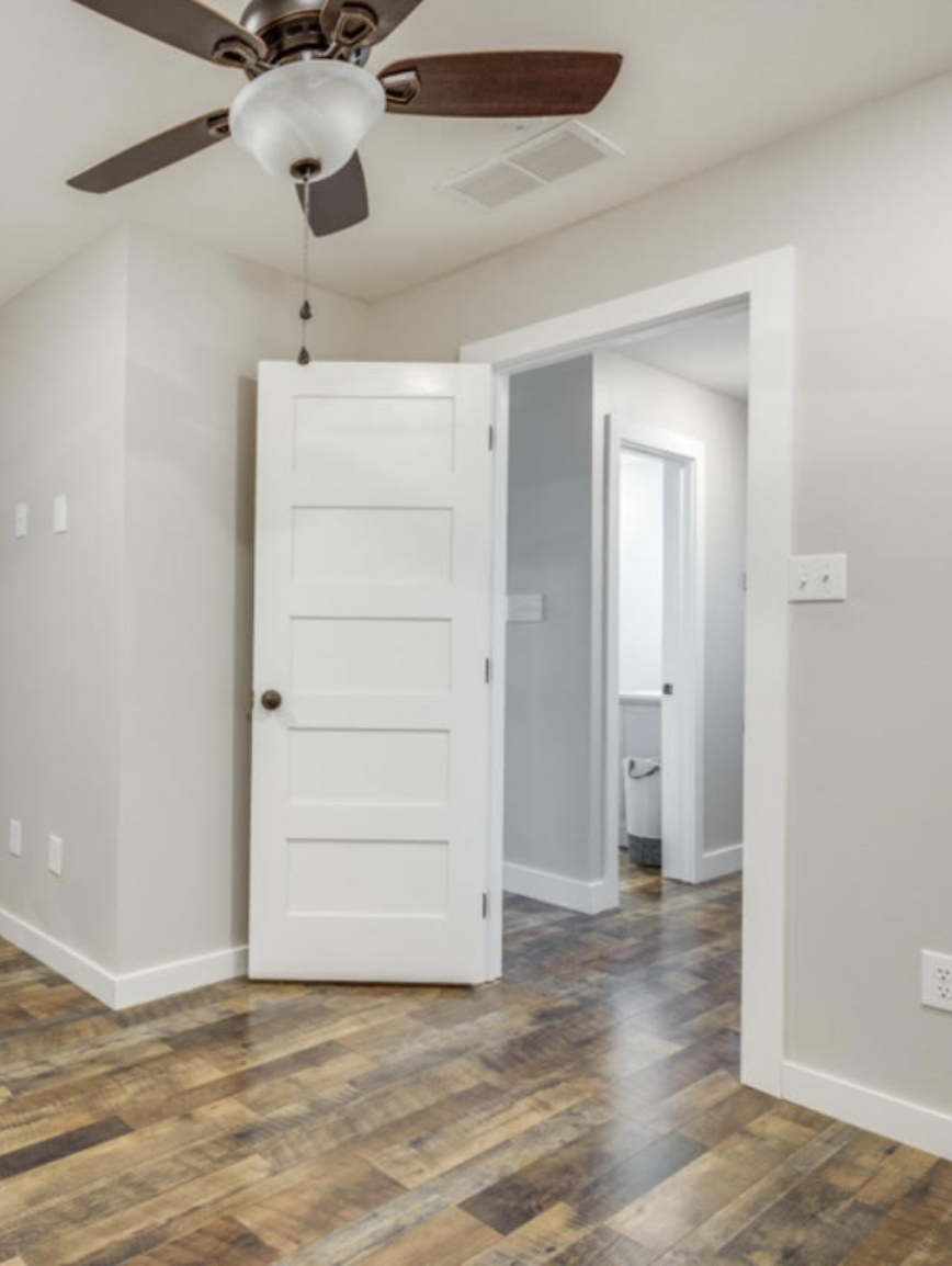 Room with hardwood floors, white walls, ceiling fan, and open door leading to a bathroom.