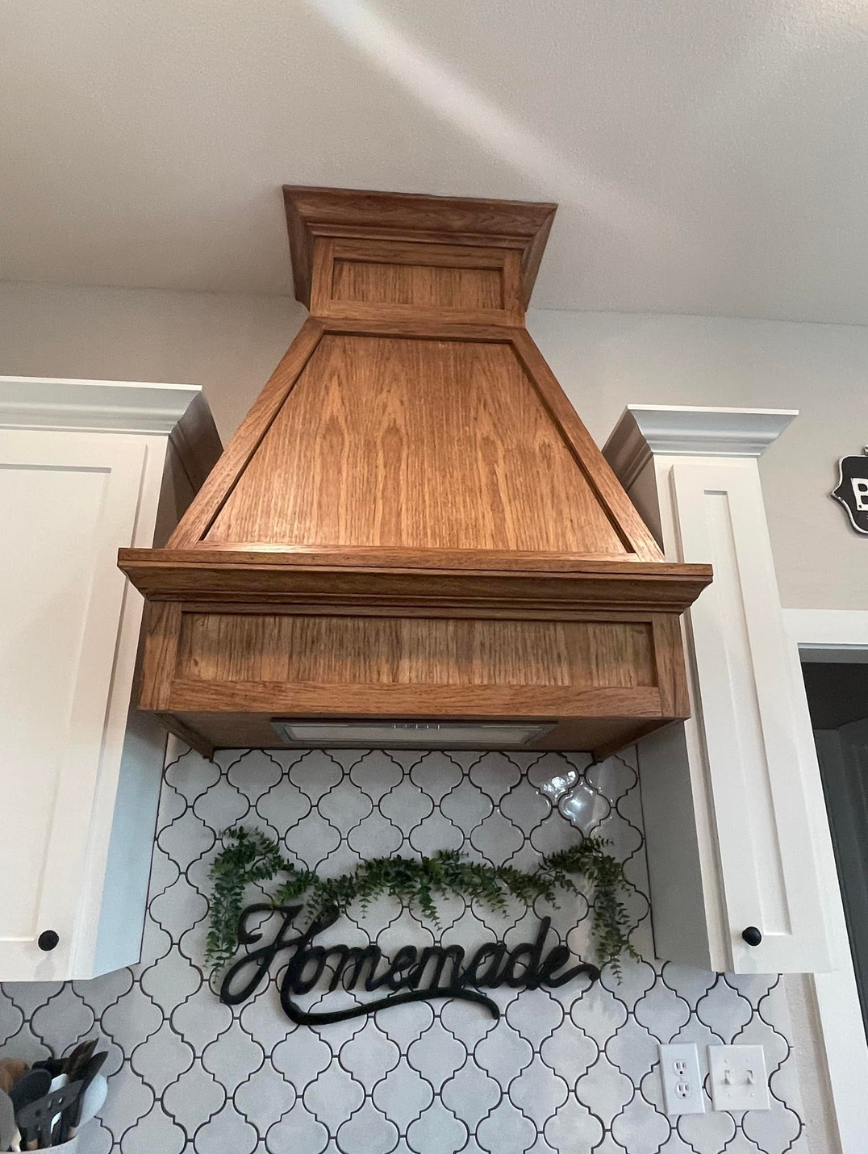 Wooden kitchen range hood above a tiled backsplash with a "Homemade" sign decorated with greenery.