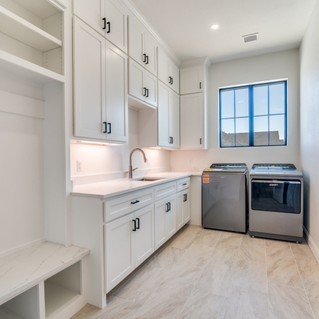 Bright laundry room with white cabinets, a stainless steel sink, a faucet, a large window, and a washer and dryer.