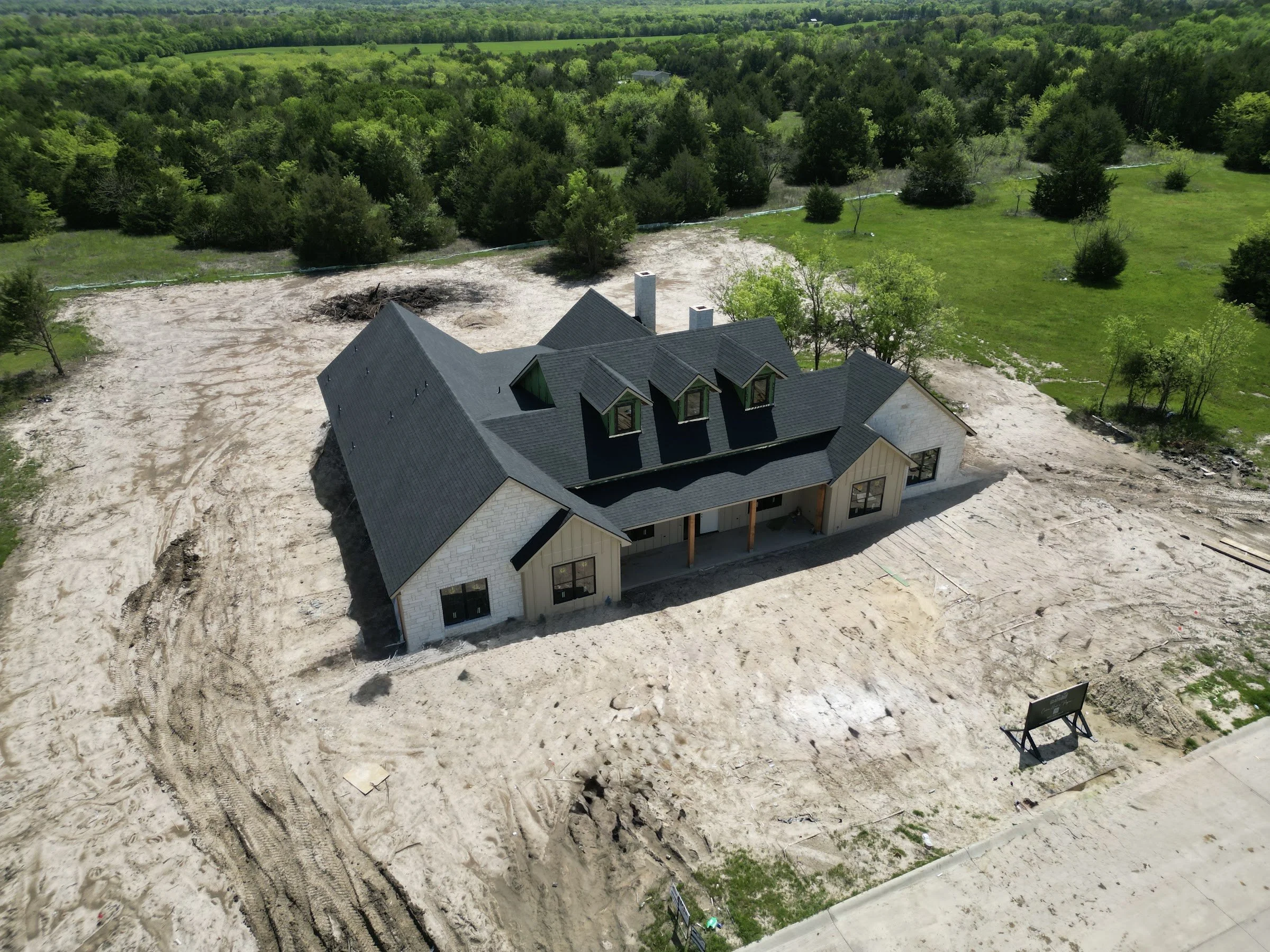 Aerial view of a North Texas custom home on a graded dirt pad showing site work and drainage before landscaping