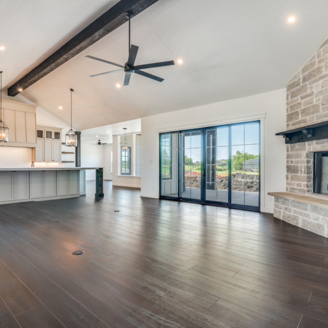 Empty living room with dark wood floors, white walls, a stone fireplace, and large sliding glass doors leading outside.