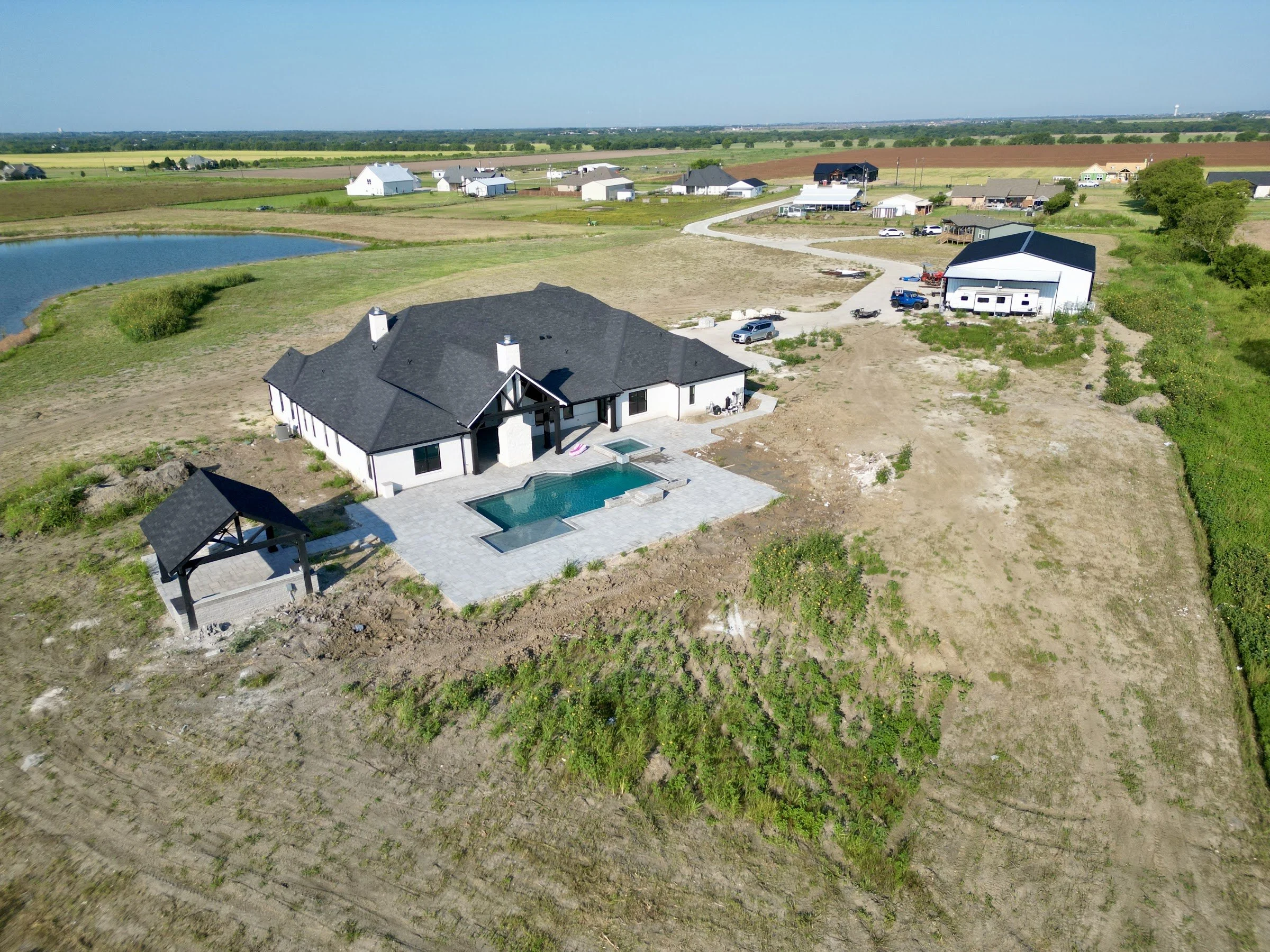 Aerial view of an acreage homesite with a custom home, pool and metal shop showing lot size and driveway runs