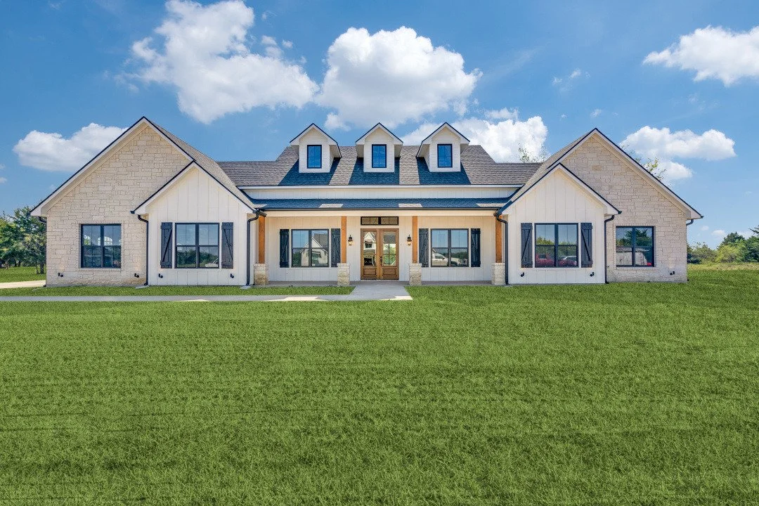 Modern house with white exterior, black window shutters, and a gray roof against a blue sky with clouds.