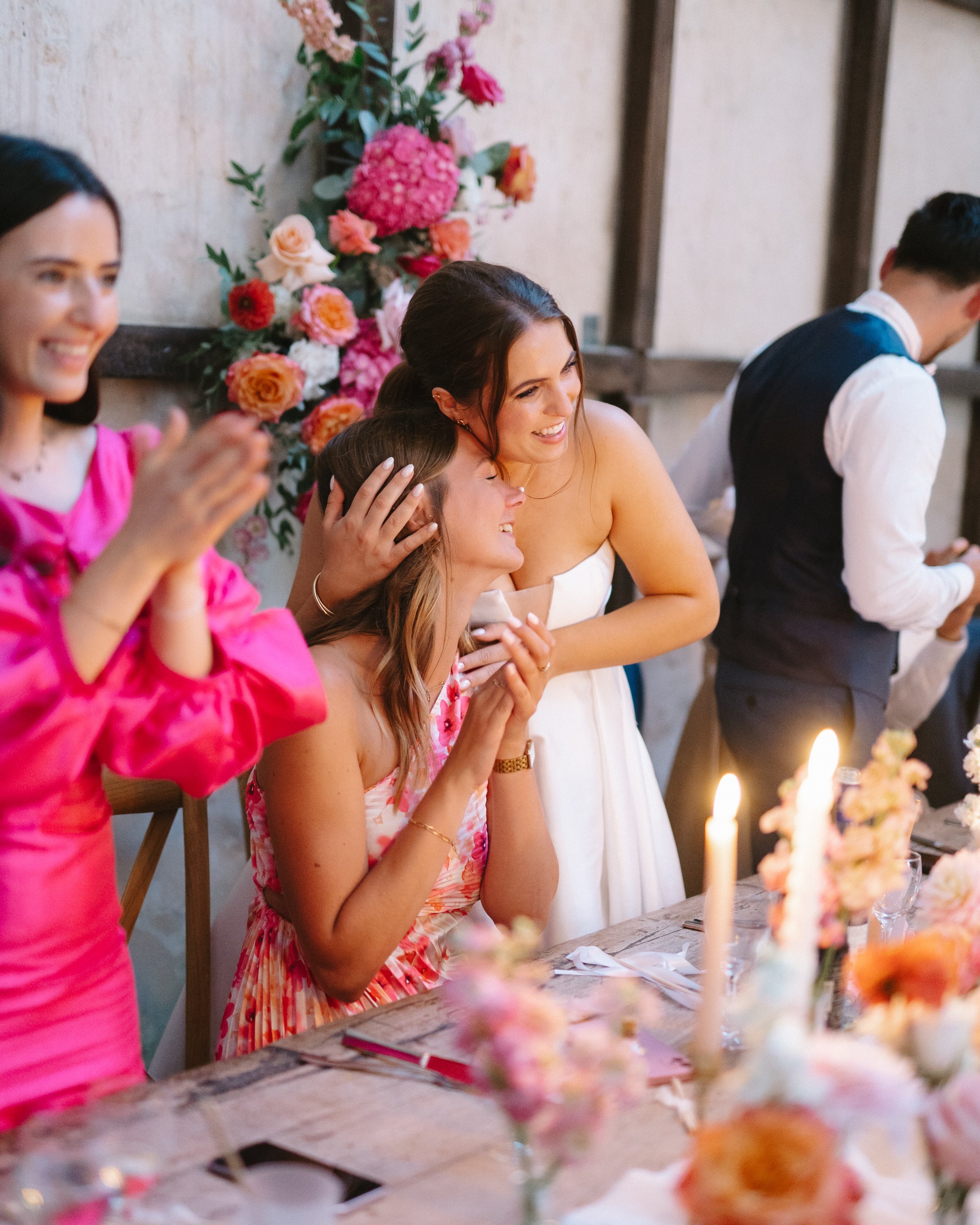 Des femmes et un homme lors d'une célébration, probablement un mariage, avec décor floral et bougies sur la table.