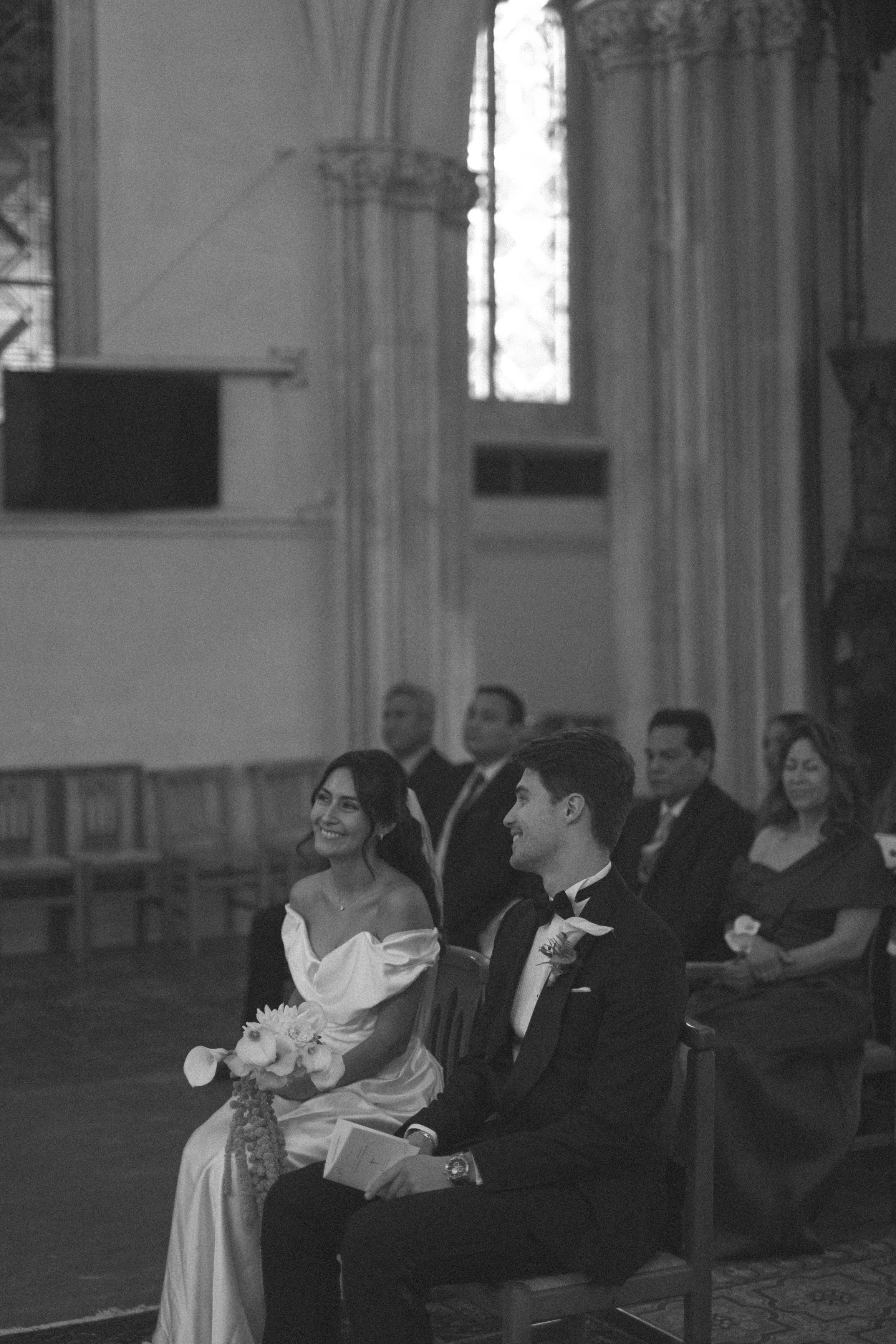Un couple en vêtements de mariage assis dans une église, entouré de personnes assises, lors d'une cérémonie de mariage.