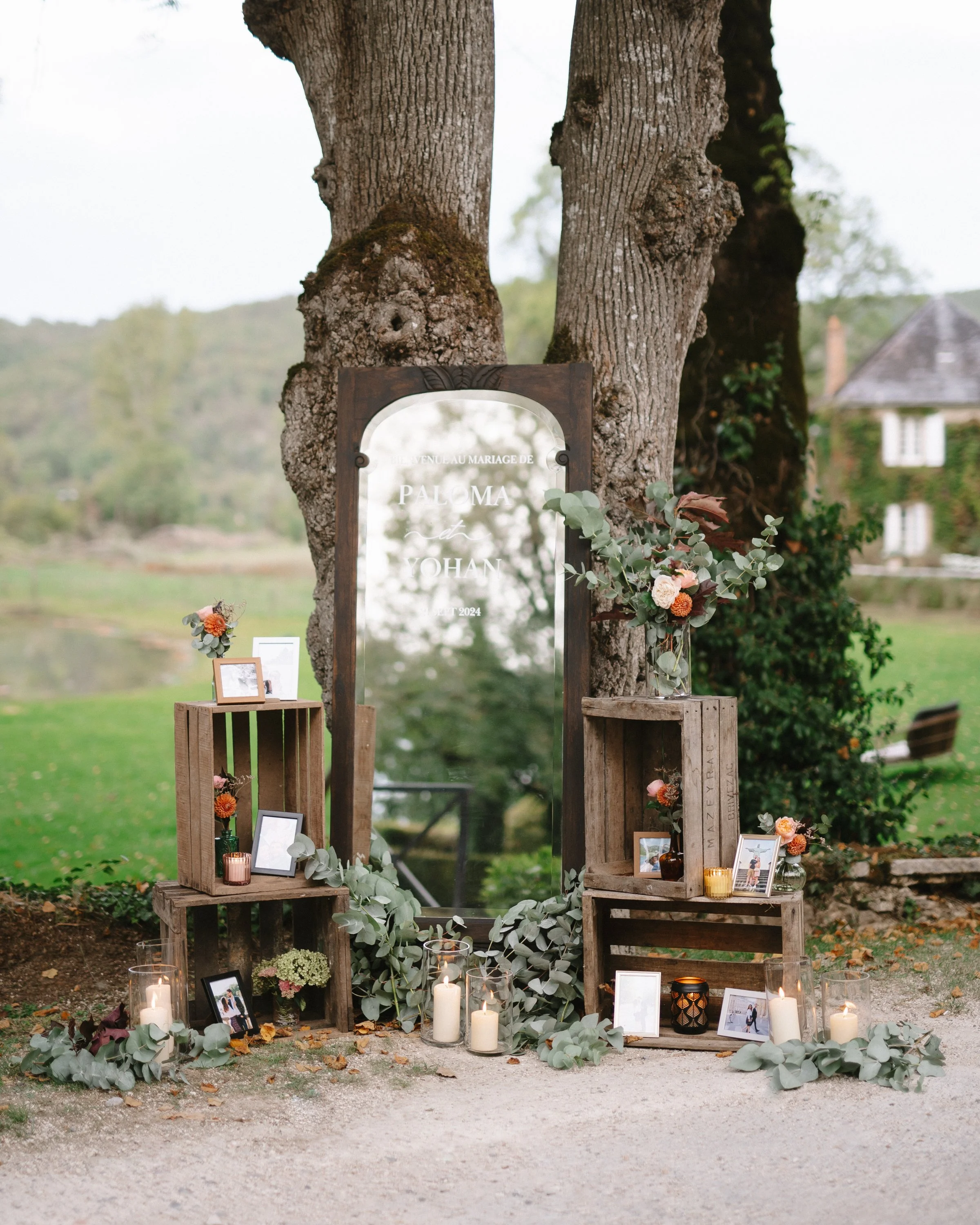 Décoration de mariage en plein air avec un grand miroir, bouquets de fleurs, bougies et cadres photos.