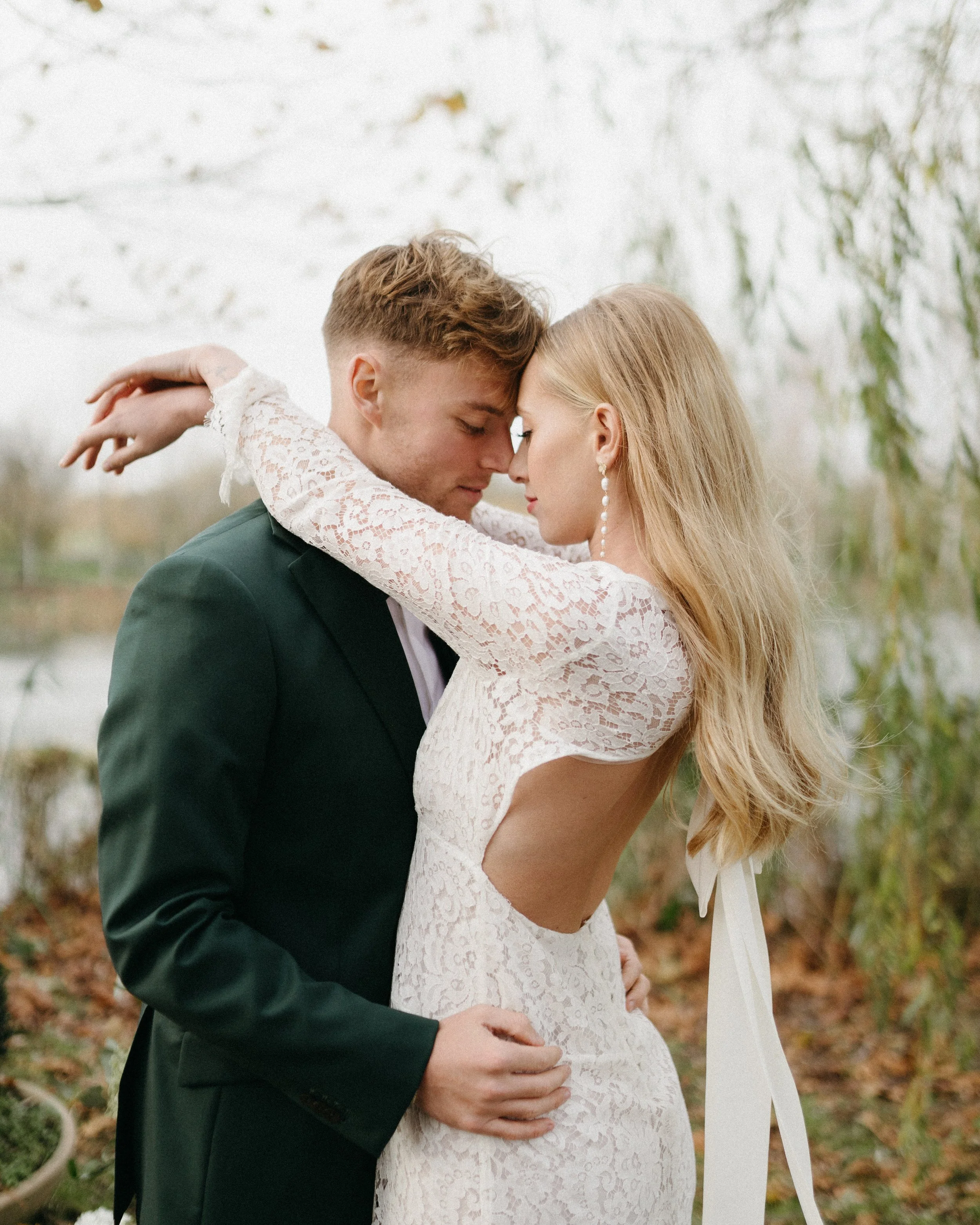 Un couple danse en plein air, avec un fond flou de nature et d'eau, lors d'une séance photo romantique.