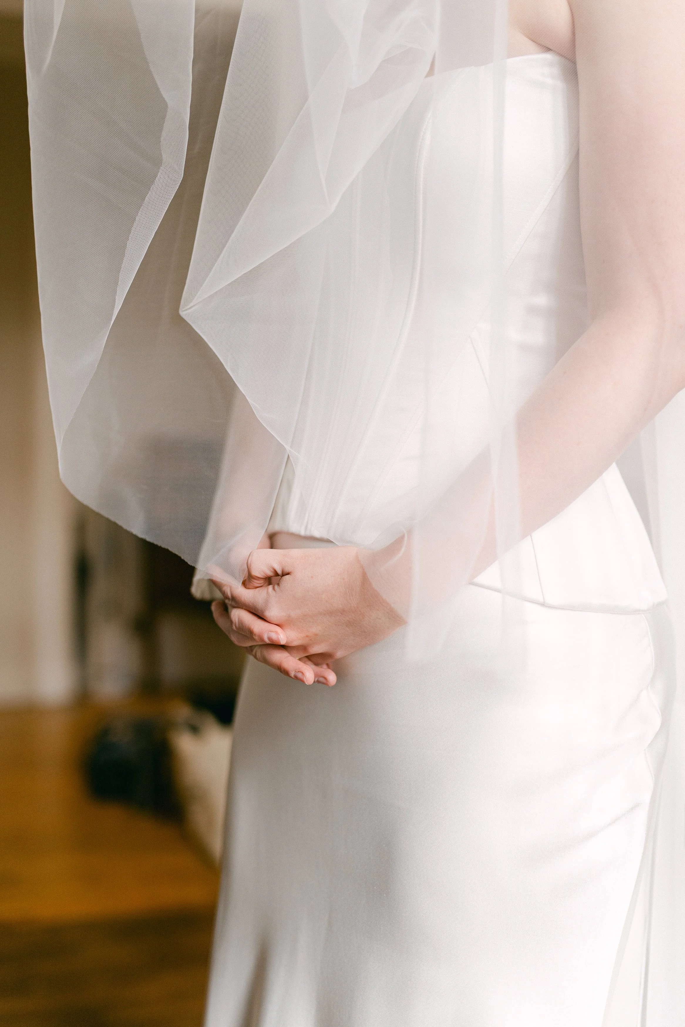 Une femme en robe blanche de mariée, tenant ses mains devant elle, avec un voile transparent sur ses épaules.