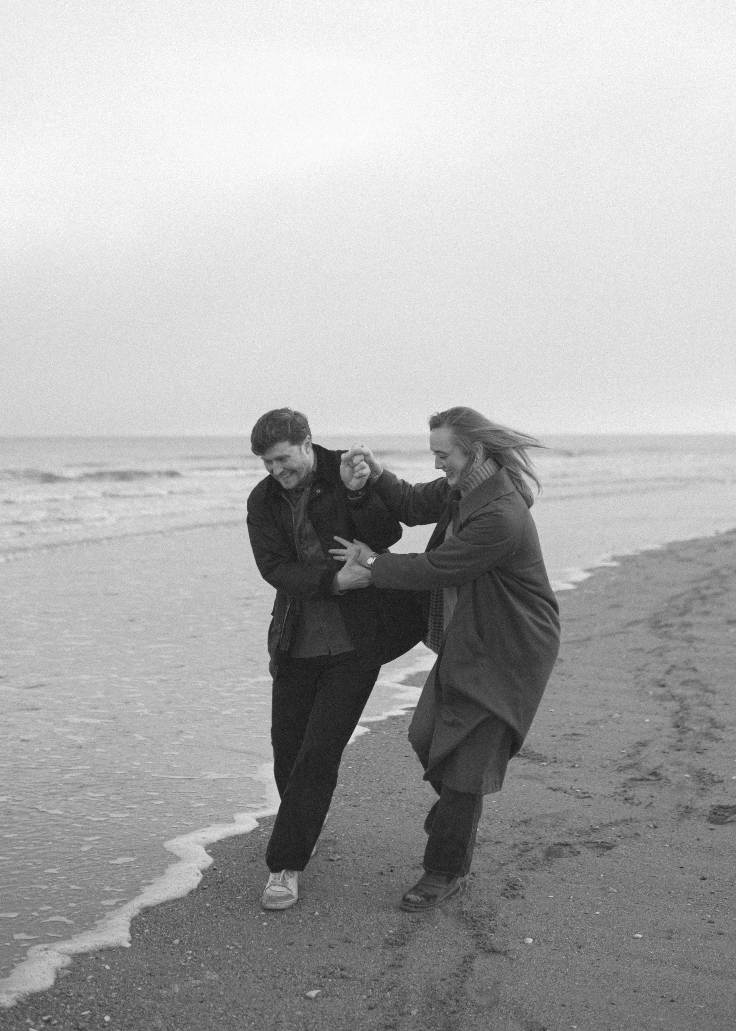 Deux personnes, un homme et une femme, s'amusent en marchant sur la plage près de la mer, en se tenant la main et en riant ensemble.