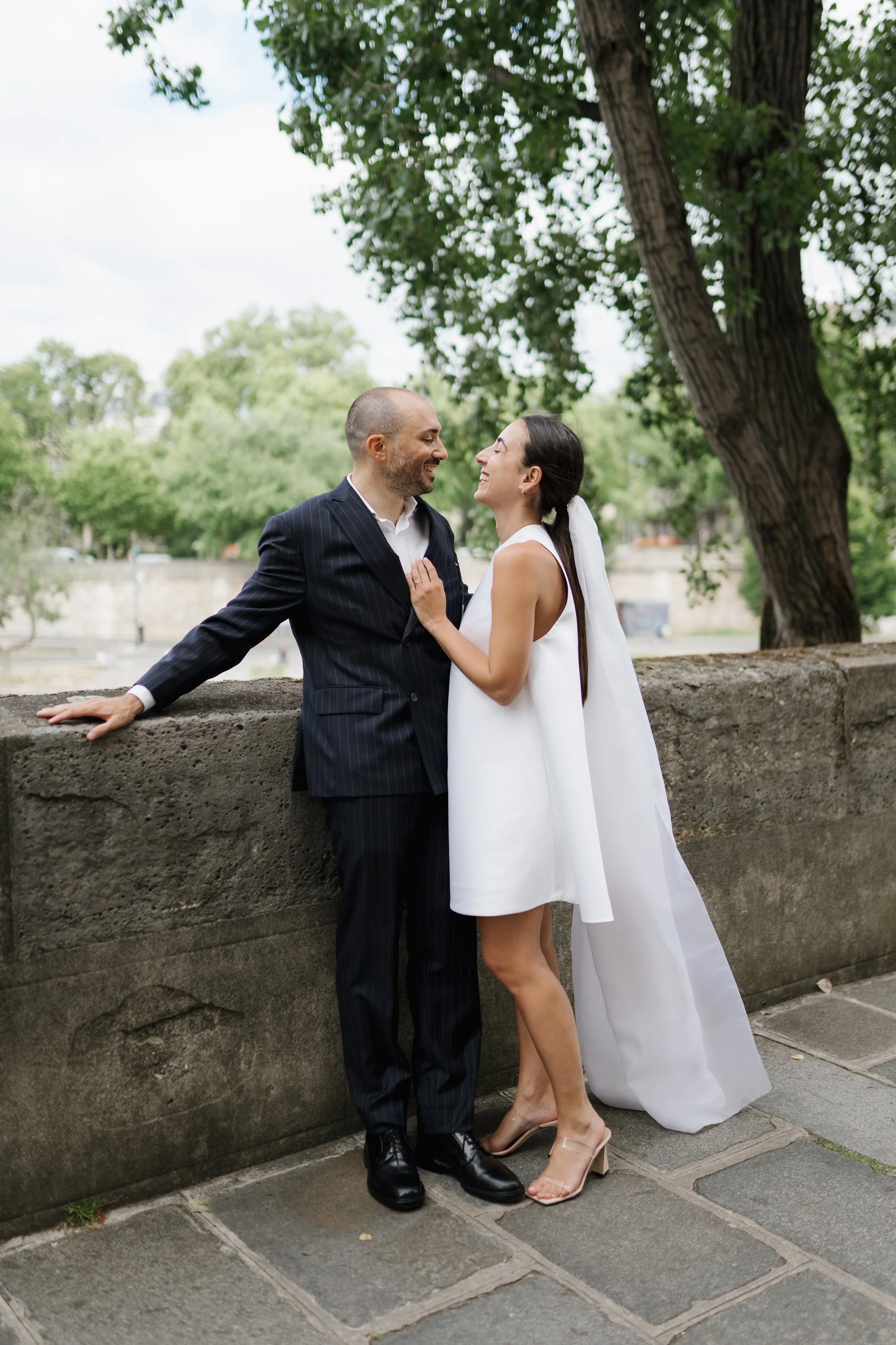 Un couple habillé en élégant, s'apprêtant à s'embrasser ou à se faire un câlin dans un parc, avec des arbres verts en arrière-plan.