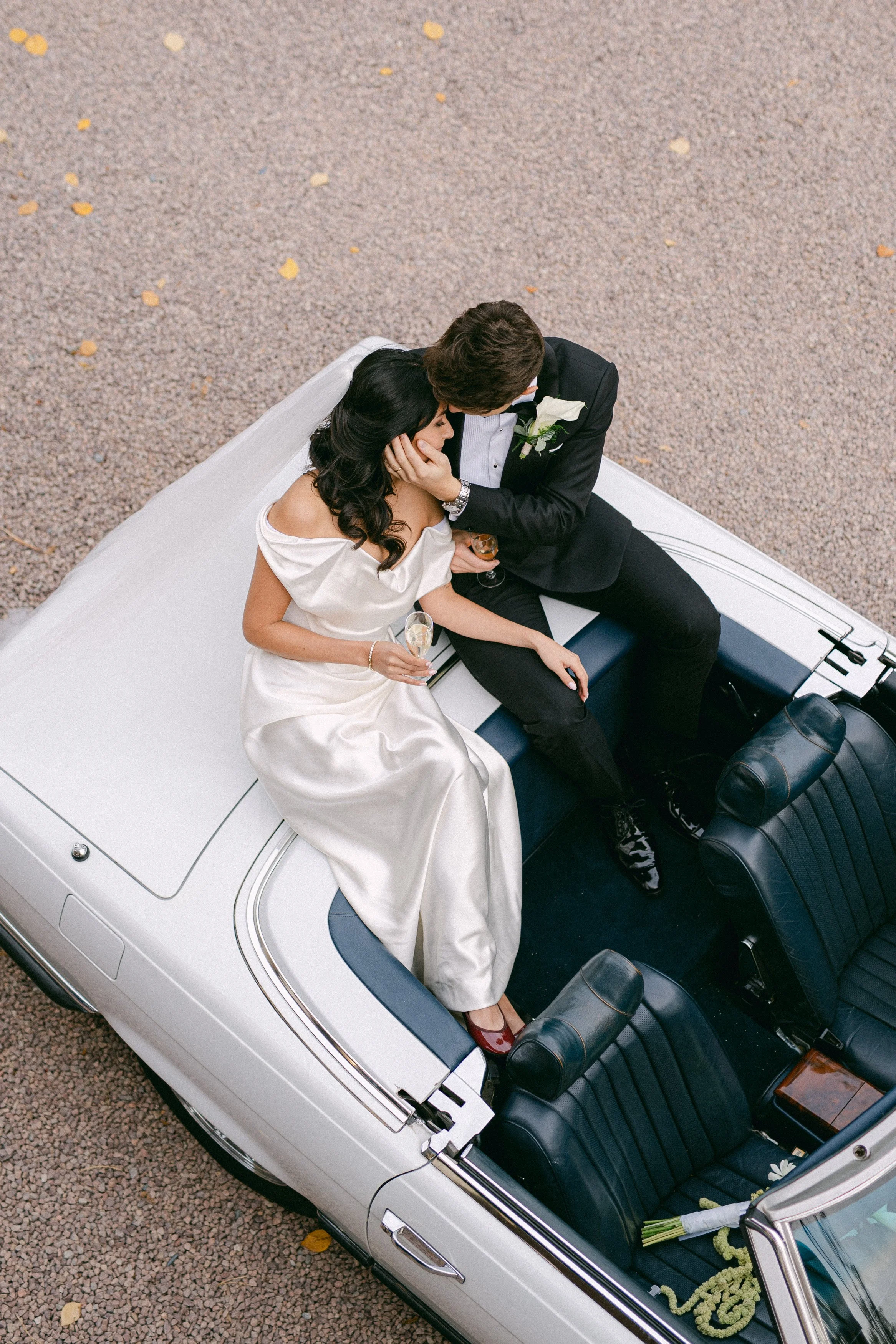 Un couple marié assis dans une voiture décapotable, partageant un moment intime et anniversaire, tenant des verres de champagne.