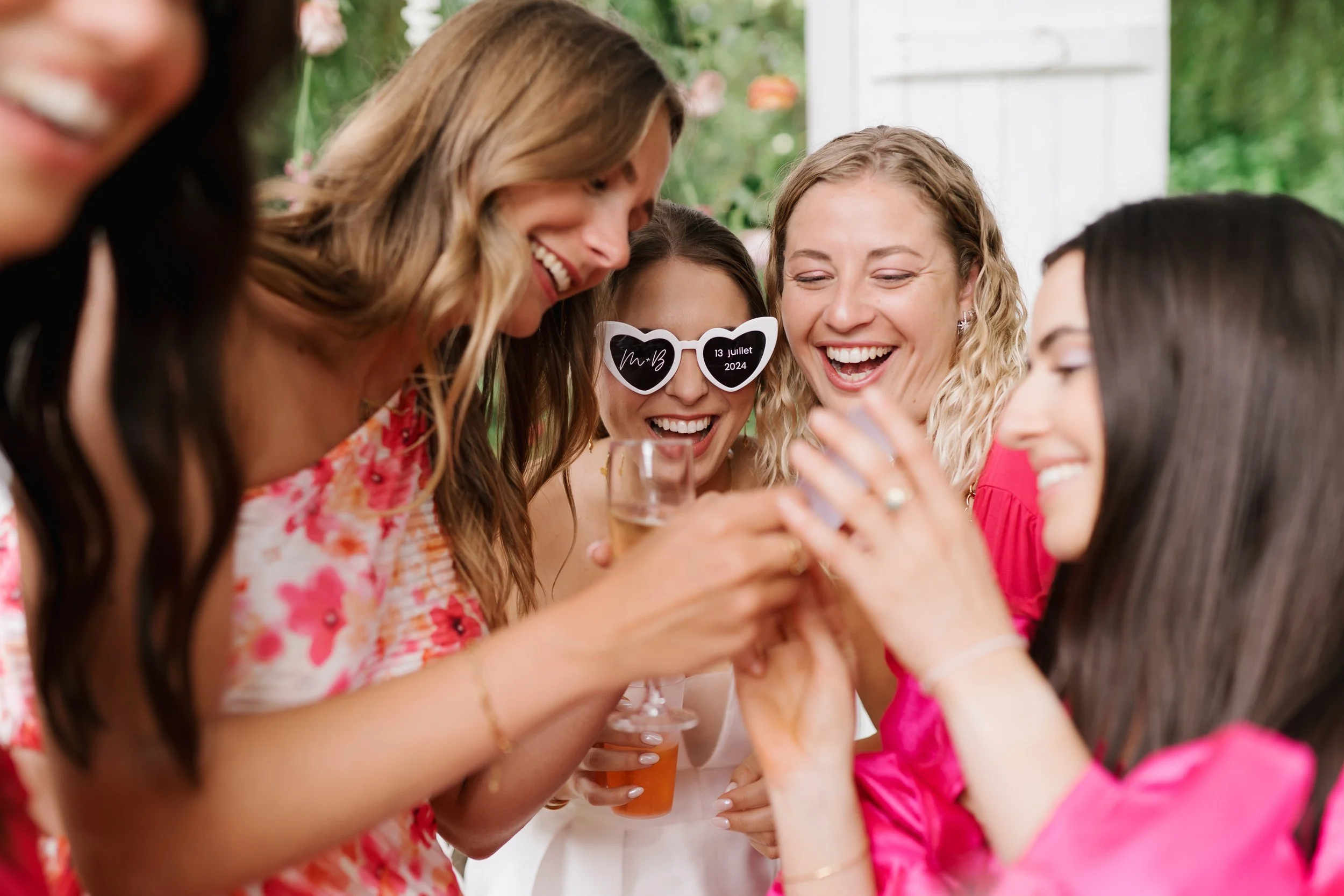 Groupe de femmes souriantes, portant des tenues colorées, qui trinquent lors d'une célébration en extérieur.