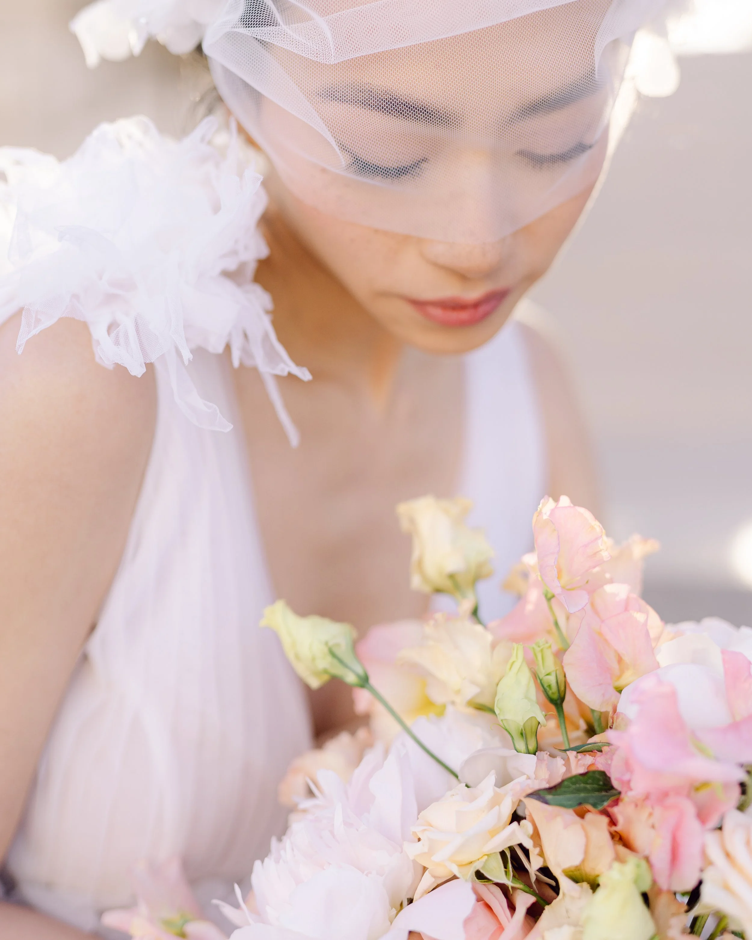 Une jeune femme portant un voile de mariée, tenant un bouquet de fleurs pastel dans un cadre lumineux.
