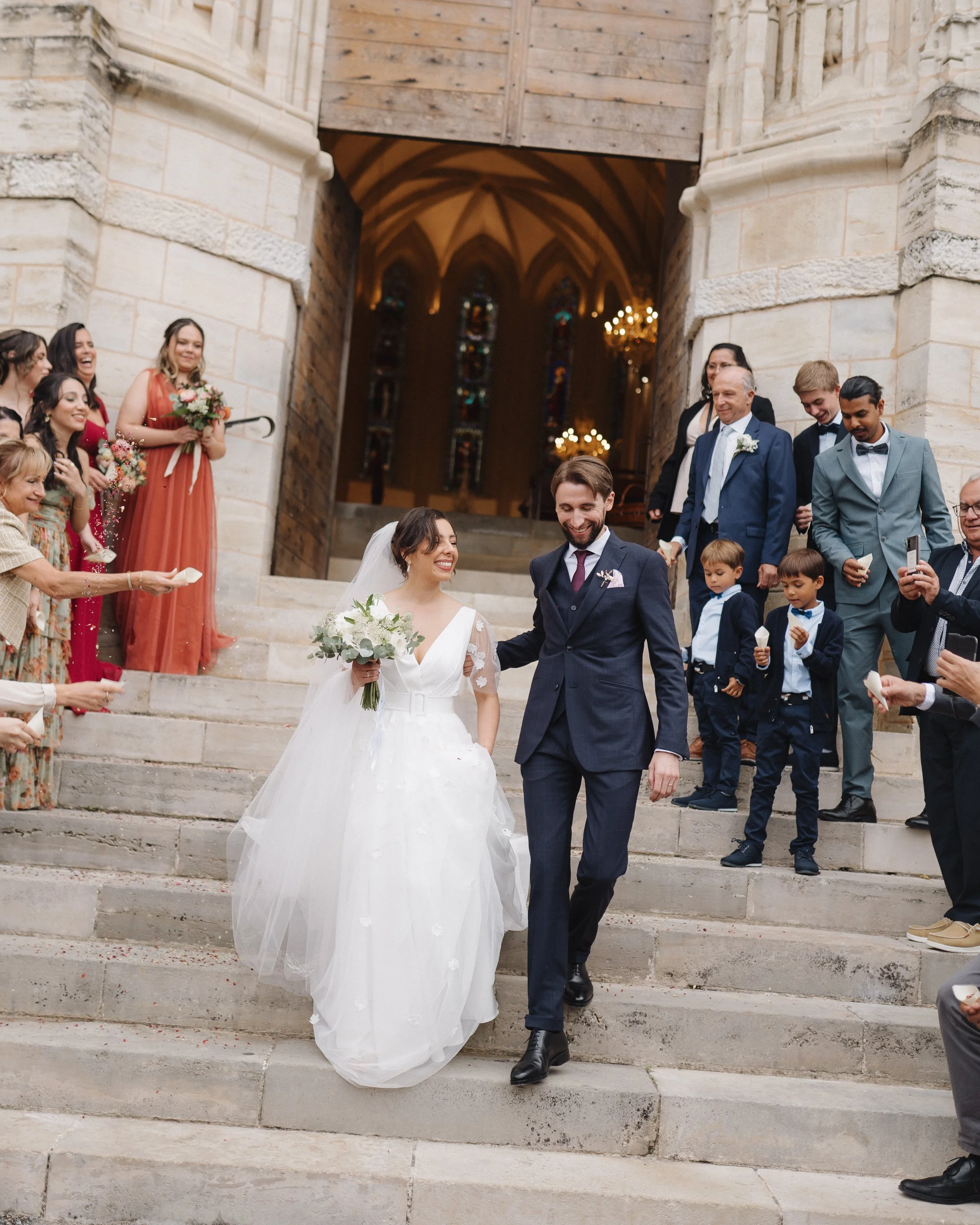 Un couple de mariés descend les escaliers de l'église entouré de familles et amis, célébrant leur mariage.