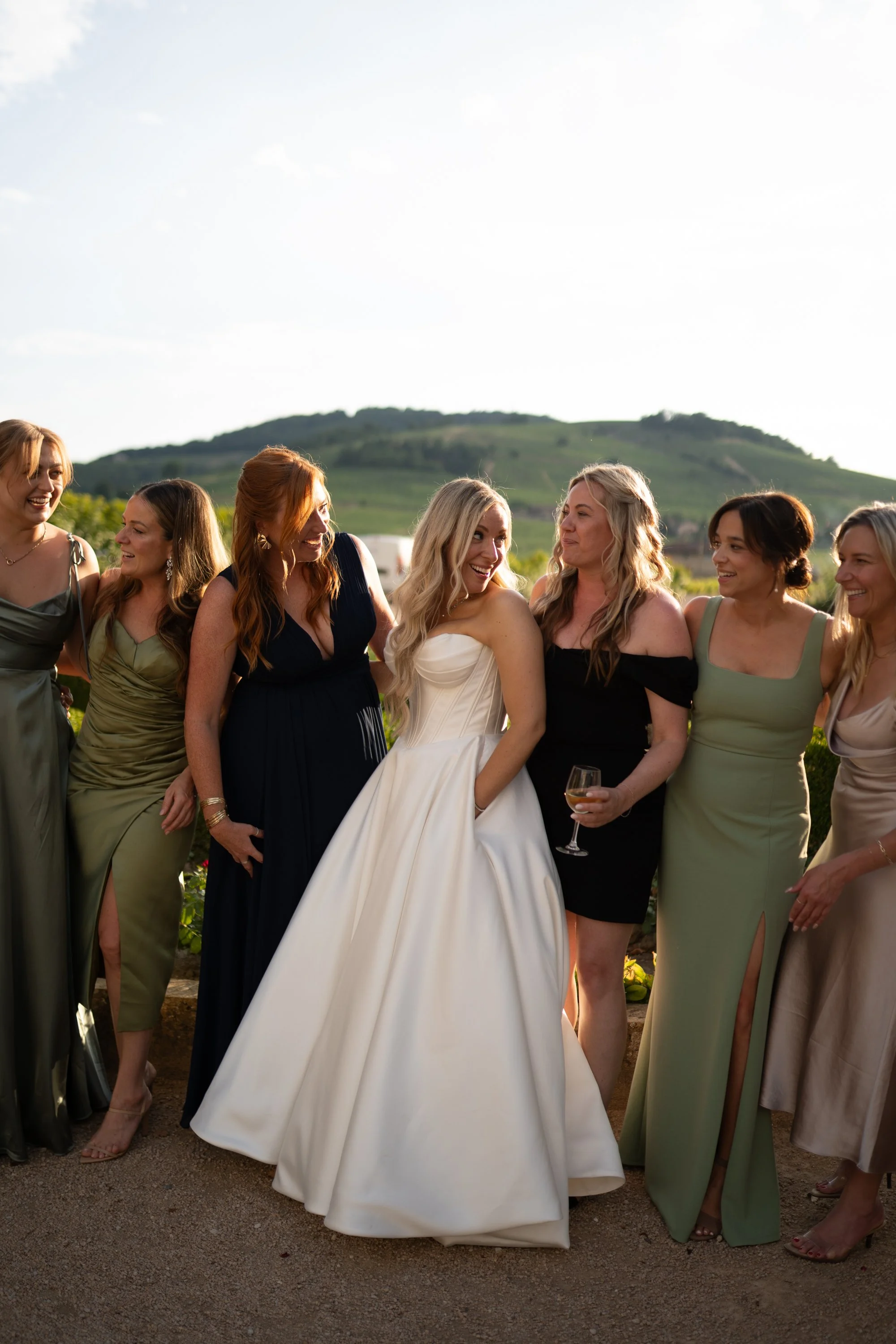 Groupe de femmes en robes de soirée, dont une femme en robe de mariée blanche, souriant lors d'une sortie en extérieur.