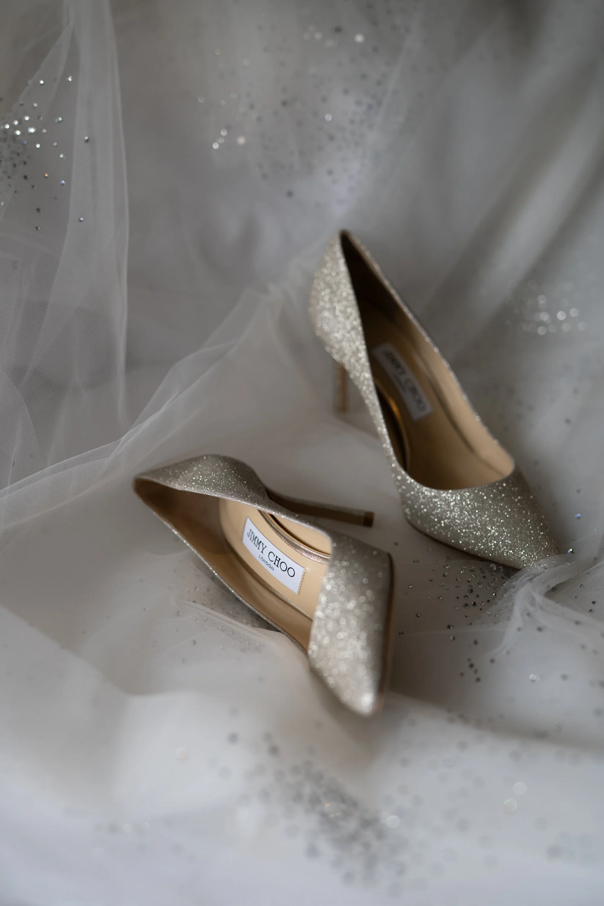 Chaussures à talons hauts dorées, recouvertes de paillettes, posées sur un tissu blanc avec des paillettes