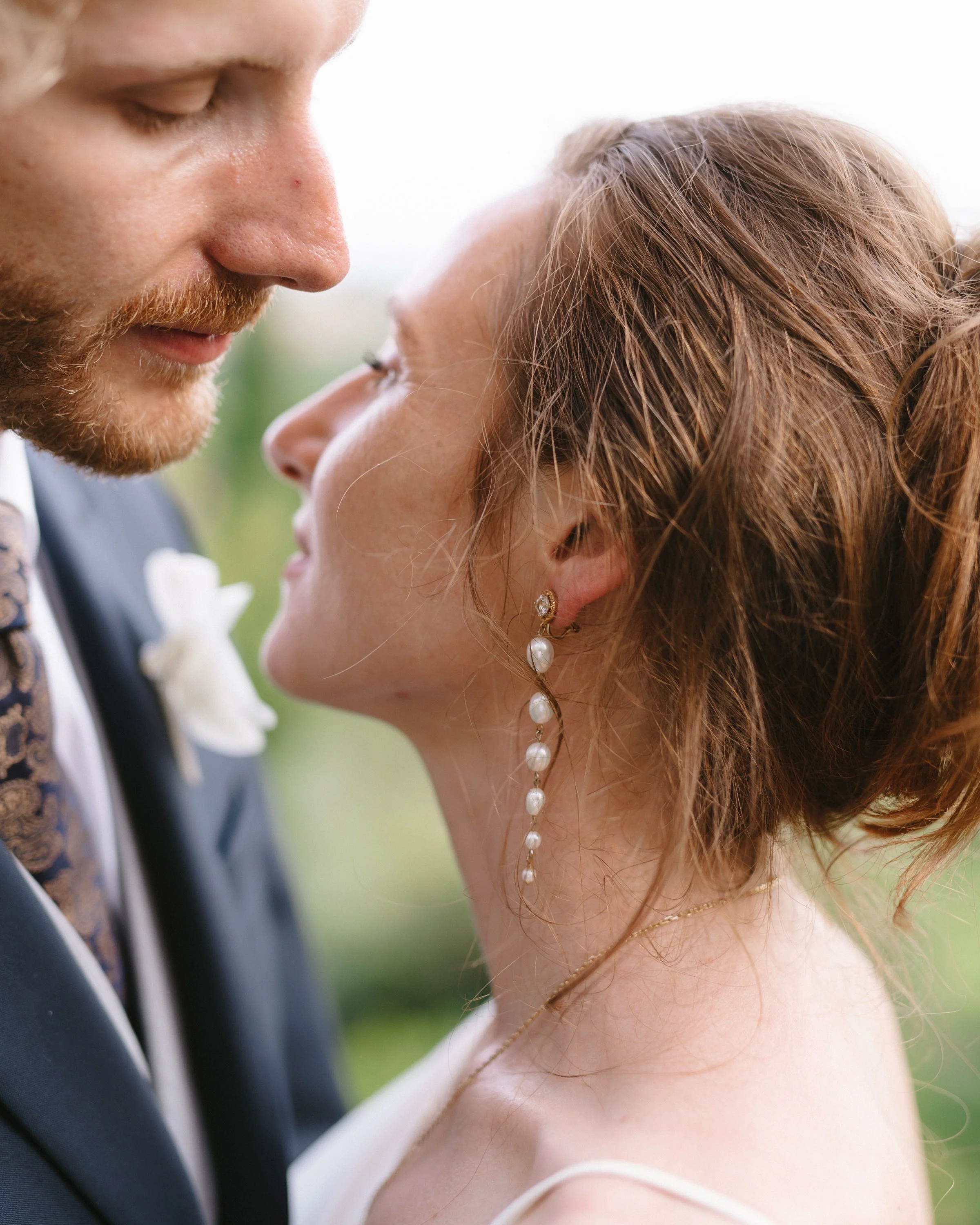 Un couple de mariés s'apprête à s'embrasser lors d'une cérémonie en extérieur, dans un décor naturel verdoyant.