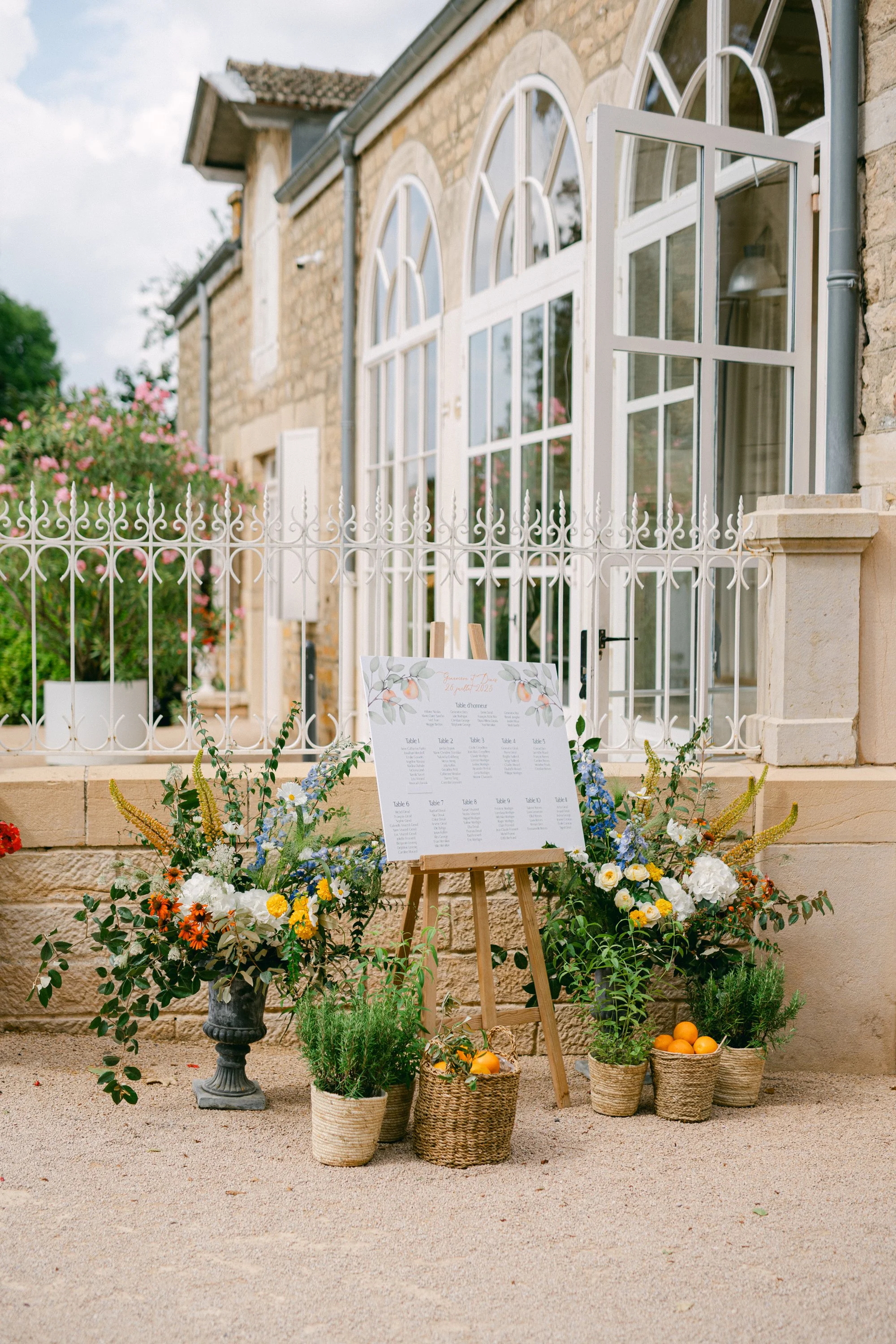 Table de mariage avec un plan et des fleurs, décorations florales et paniers d'oranges, à l'extérieur d'une maison en pierre avec un balcon en fer blanc.