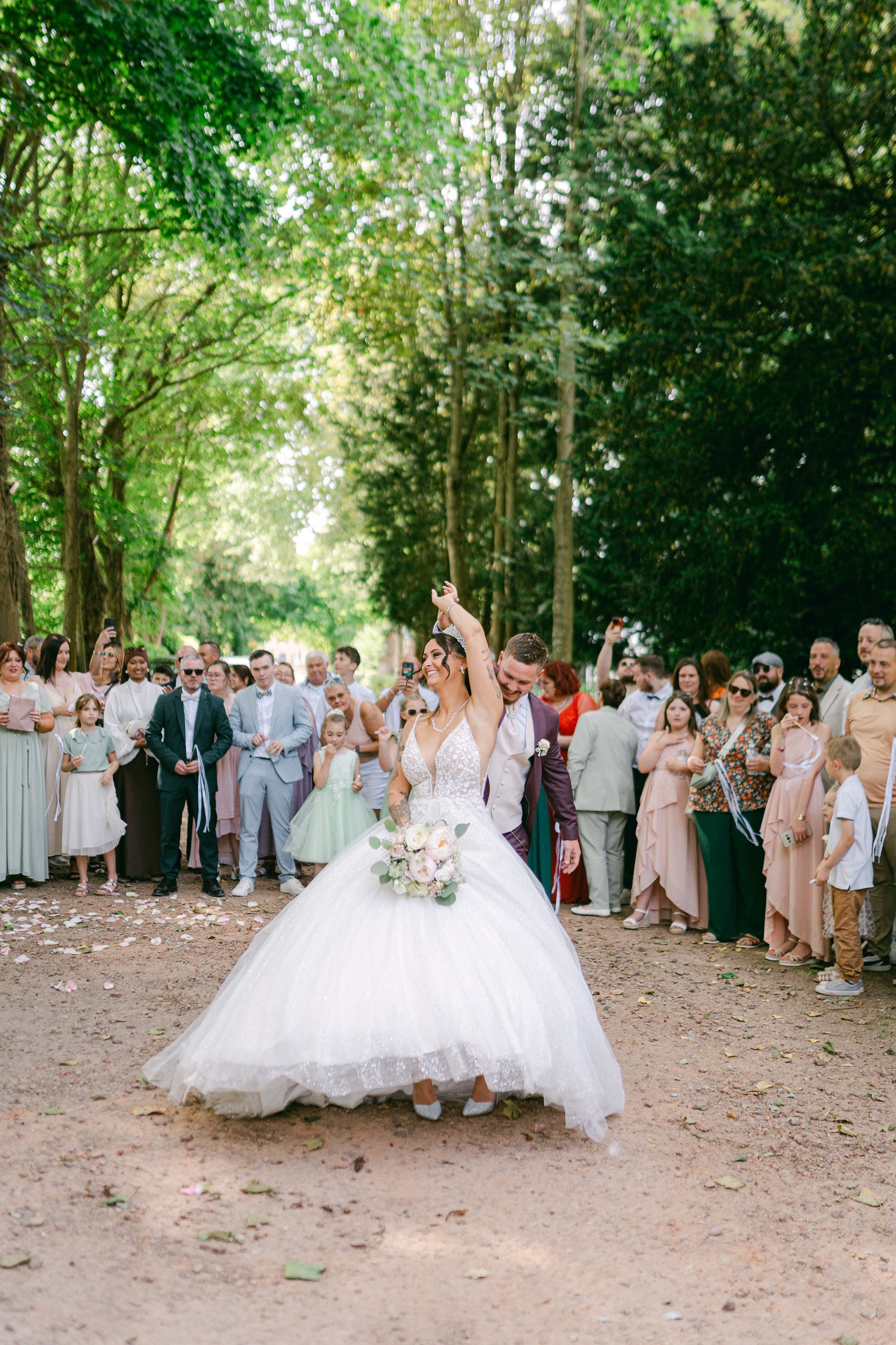 Un couple de mariés danse lors de leur mariage en plein air, entourés d'invités dans une forêt.