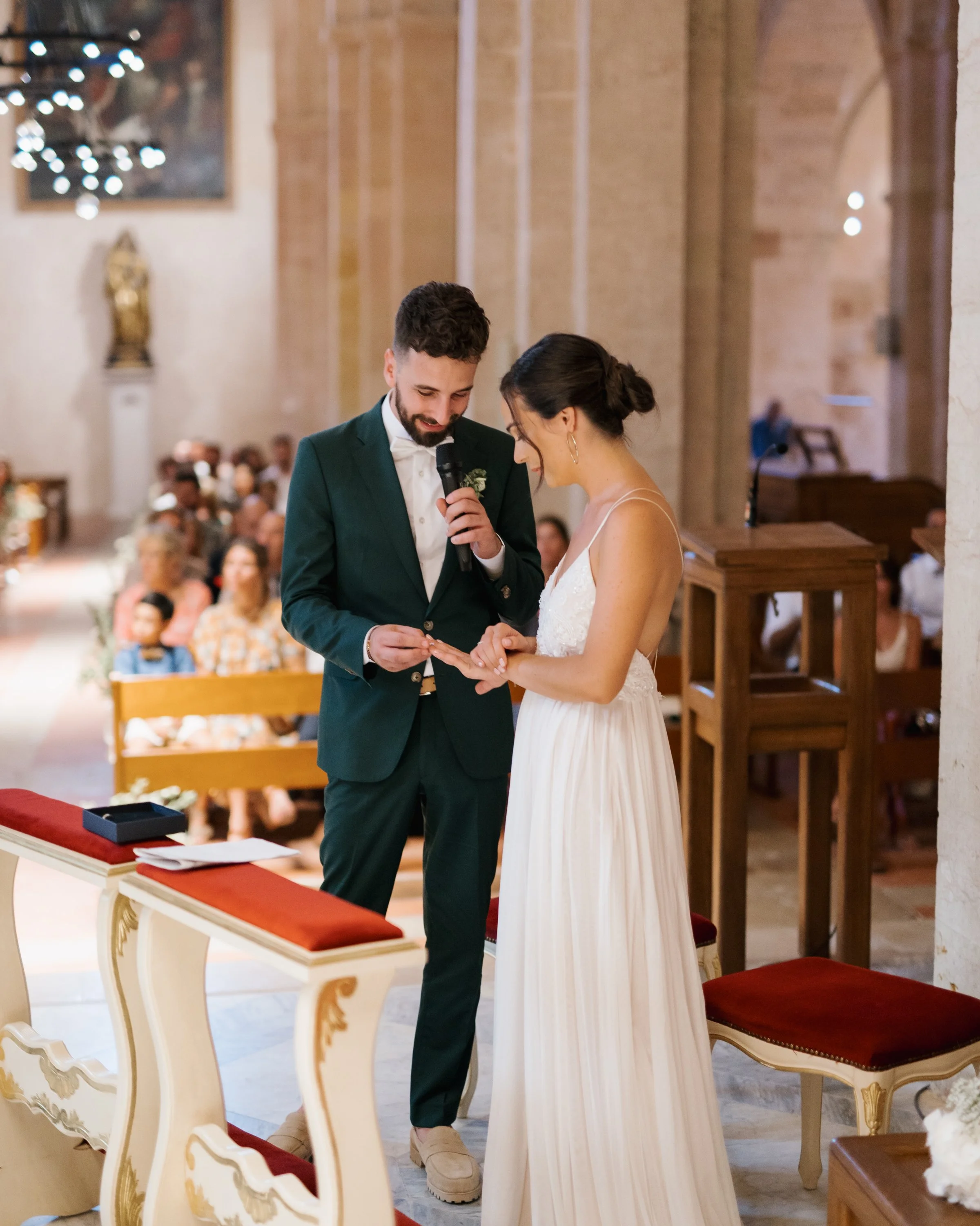 Un couple échange des vœux lors d'un mariage dans une église, entouré de invités.