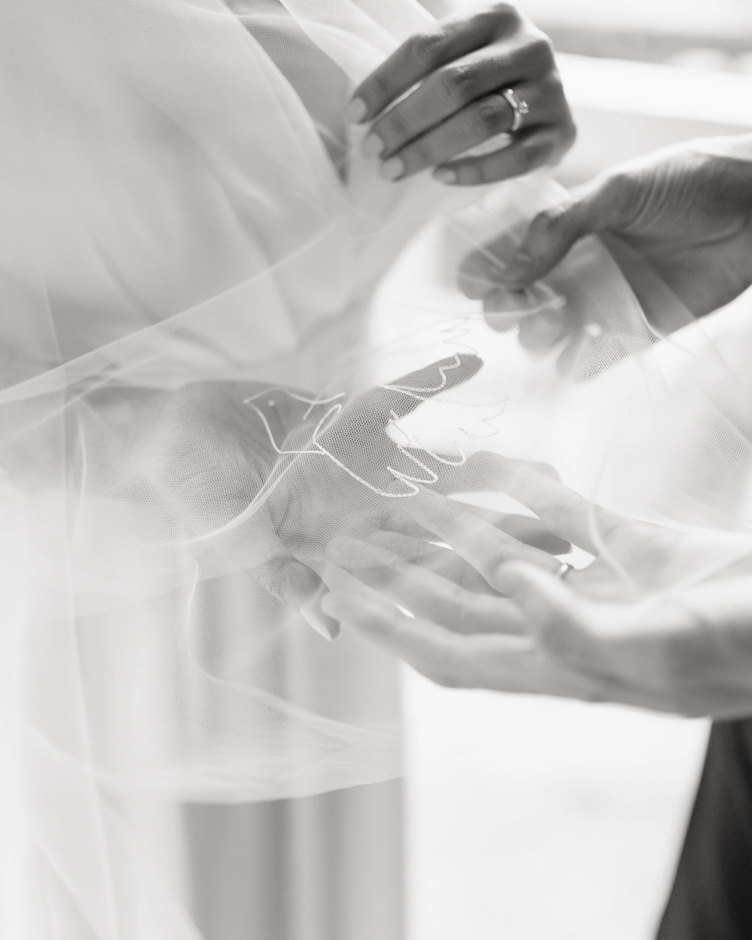 Deux mains féminines ajustent un voile de mariage en tulle délicat, avec un anneau sur l'anneau de la main gauche, dans un style en noir et blanc.