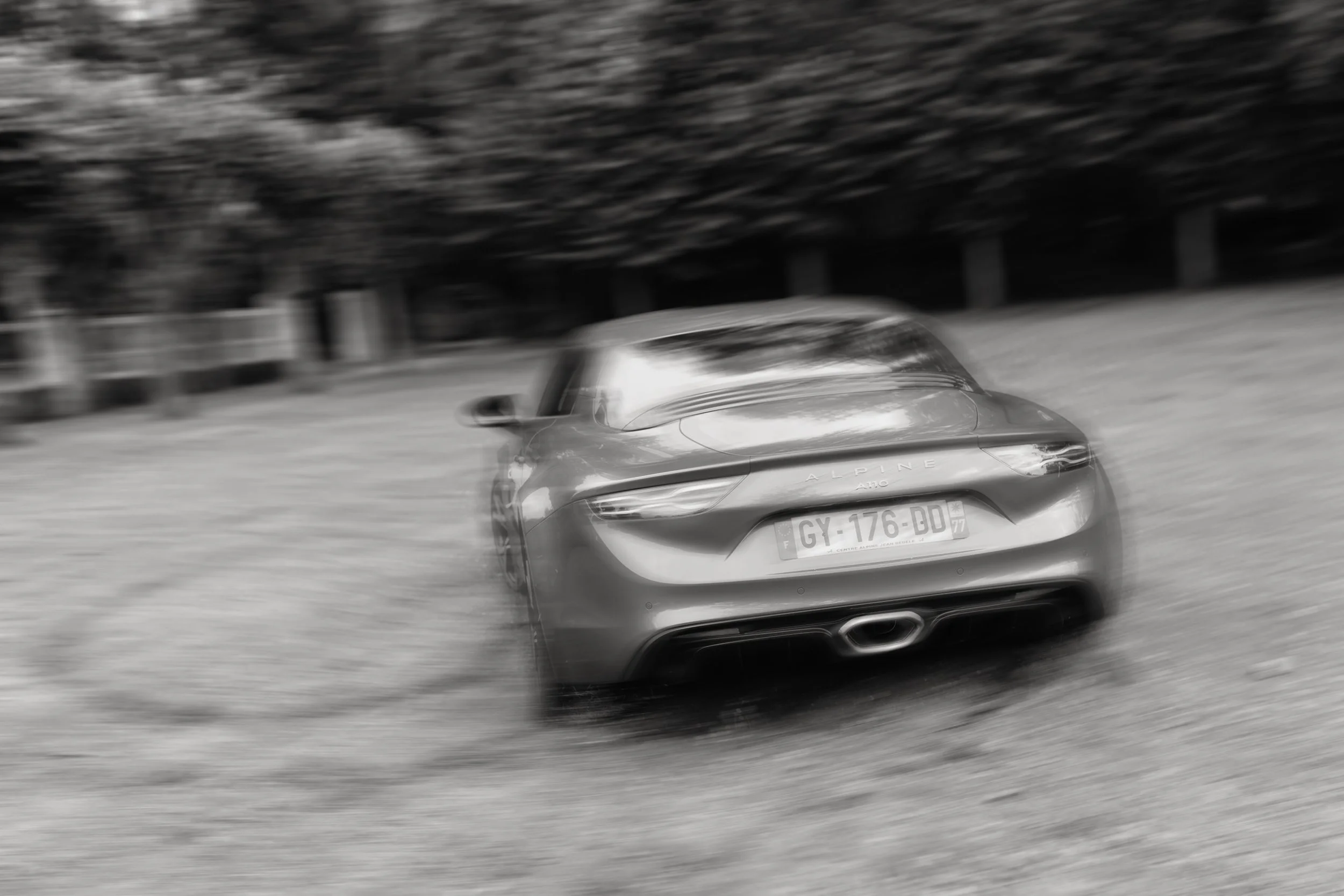 Voiture de sport moderne en mouvement sur une route, floue en arrière-plan, en noir et blanc.