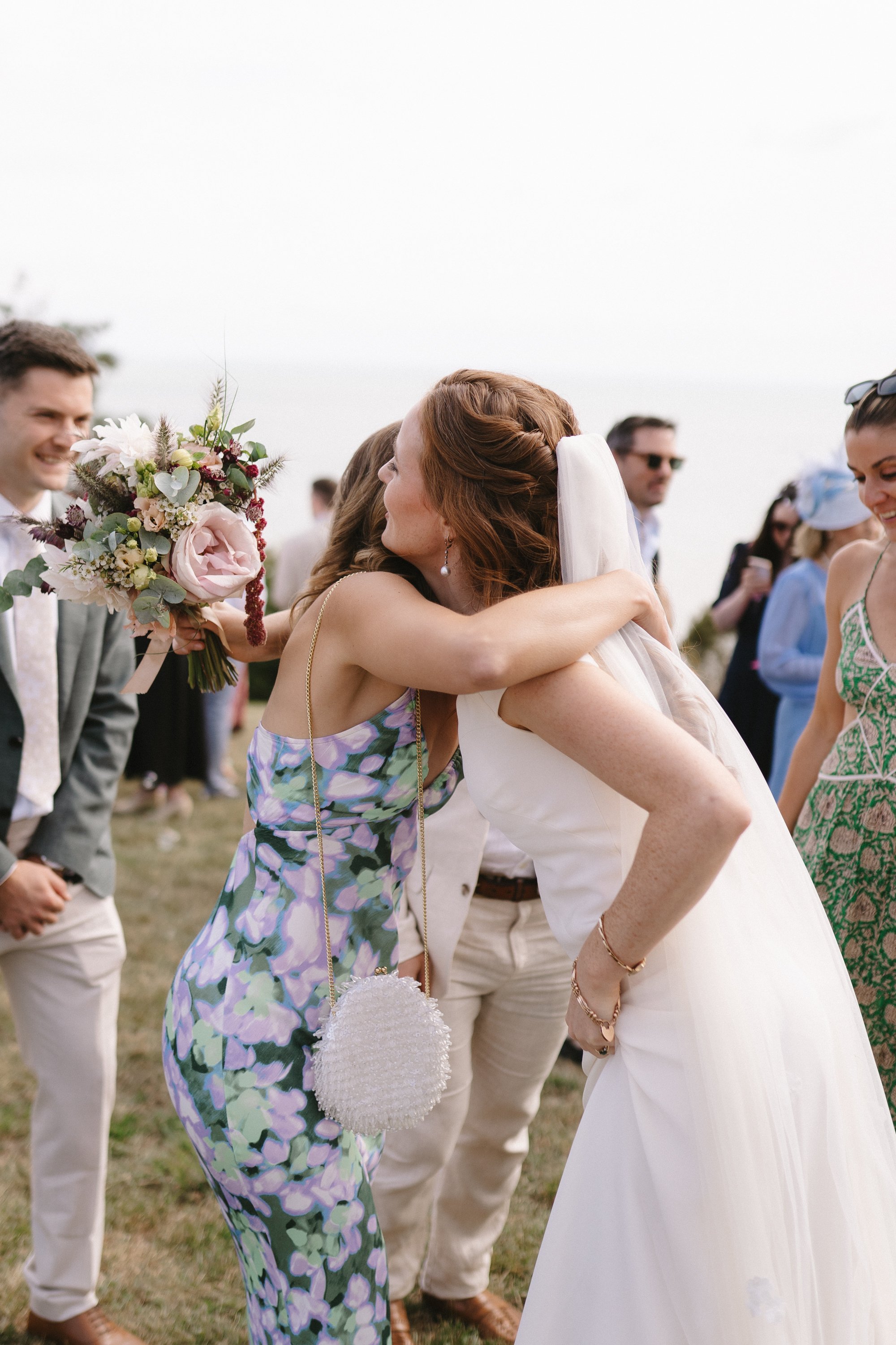 Deux femmes s'embrassent lors d'un mariage en plein air, entourées de plusieurs personnes.