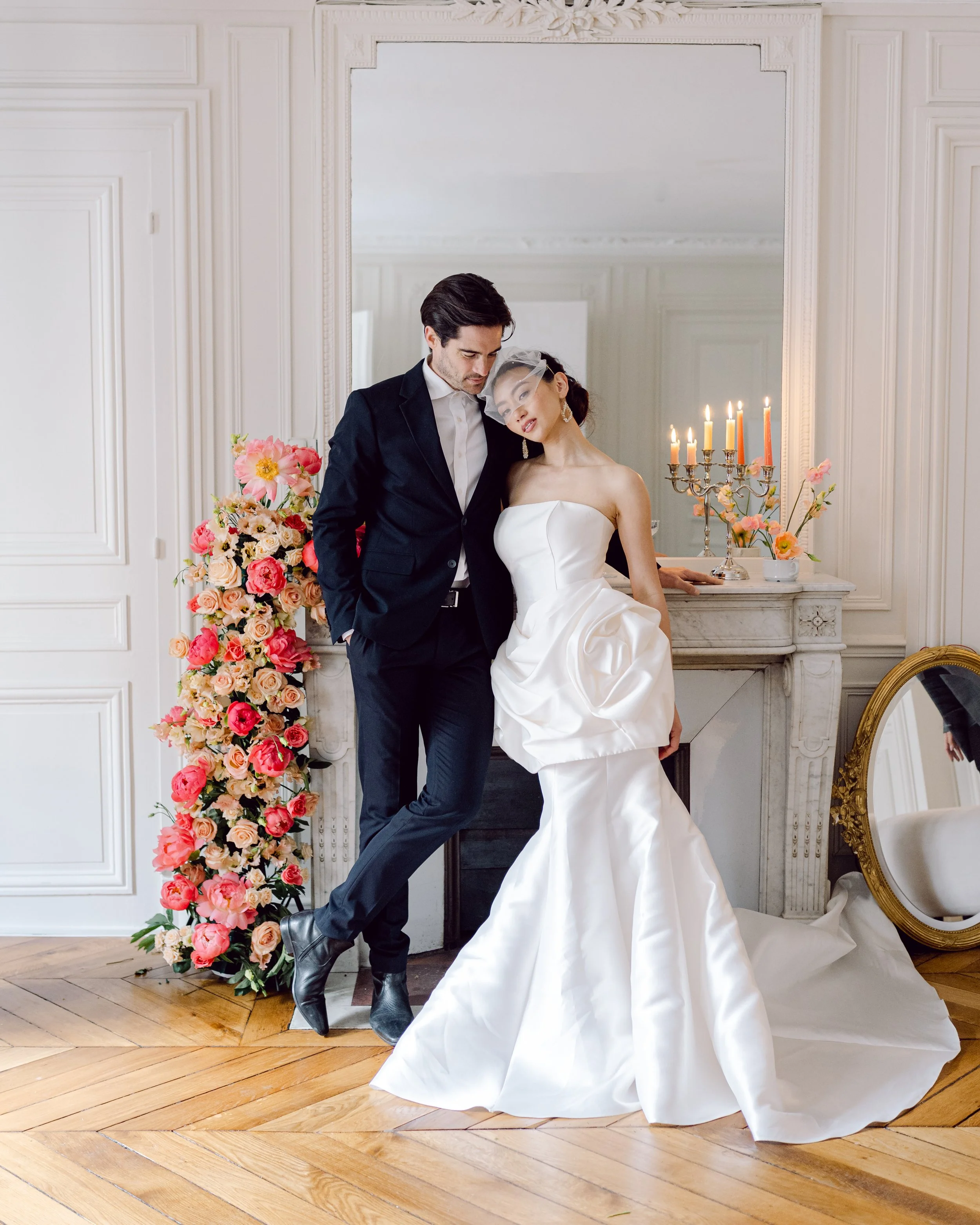 Un couple en costume de mariage pose dans une pièce élégante avec un décor floral et une cheminée.