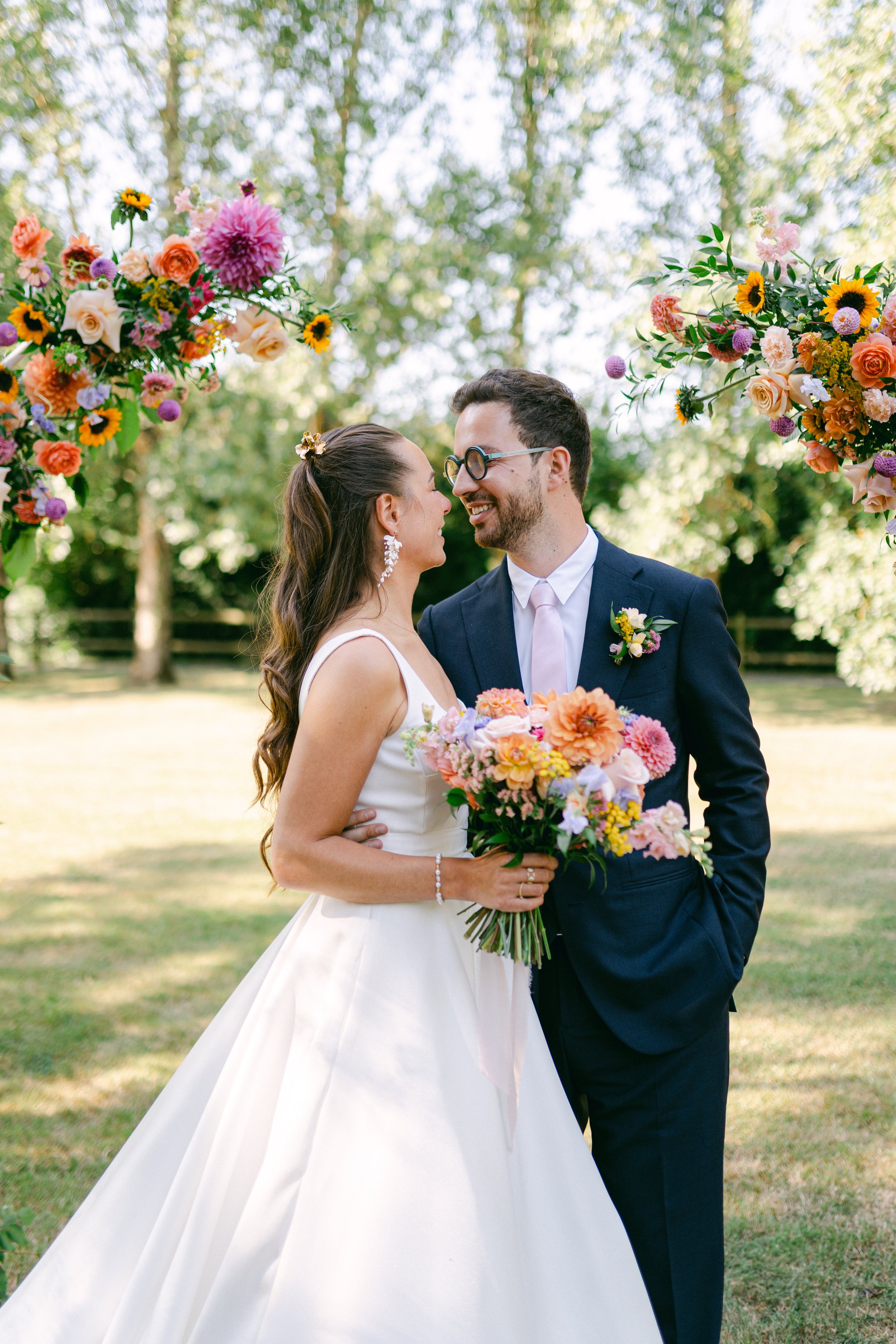 Un couple de mariés souriants à leur mariage en plein air, entouré de décorations florales colorées.
