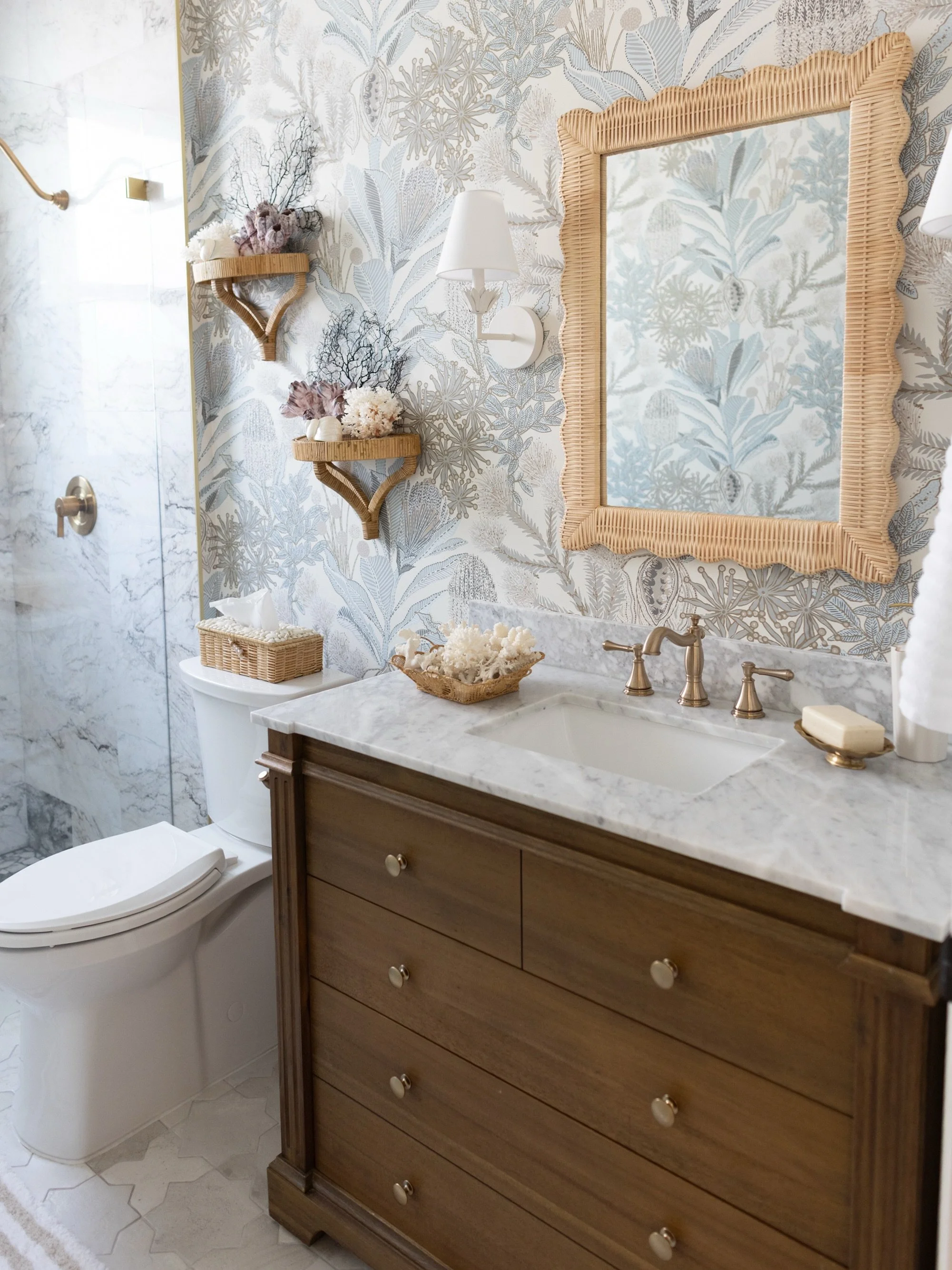 A guest bath inspired by South Floridas&rsquo; particular brand of elegance. 

With tone-on-tone marble and underwater botanical wallpaper, the dresser-style vanity adds depth and a visual anchor for the space. Finished with a scalloped rattan mirror