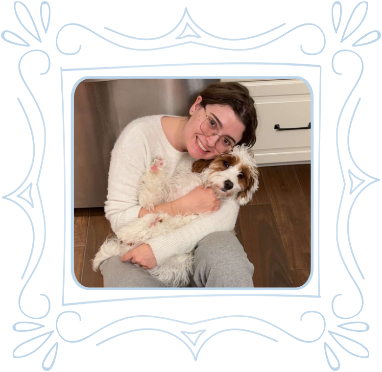 A woman with dark hair, glasses, and a white sweater smiling and hugging a white and brown dog indoors.