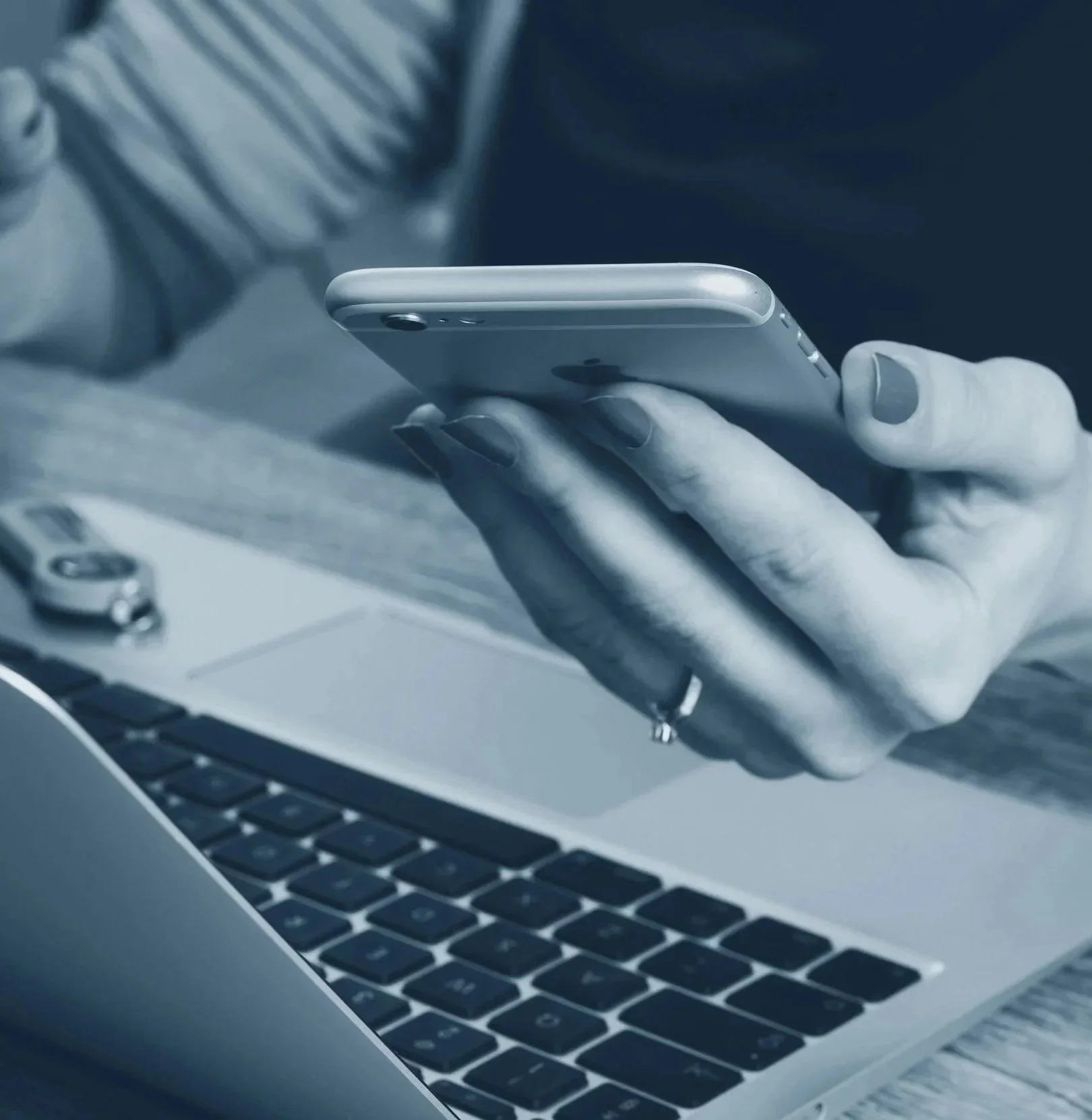 Person using smartphone while sitting at a laptop computer.