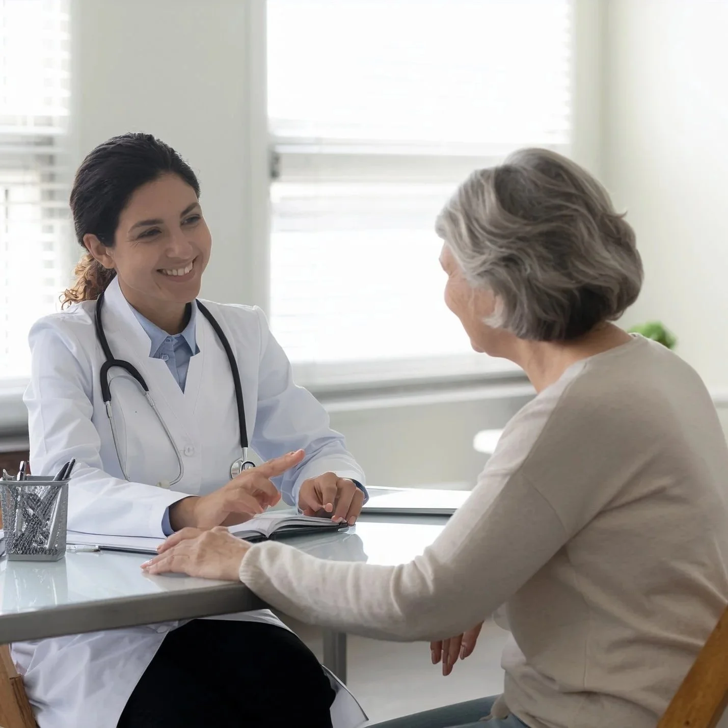 A young female doctor talking to an elderly woman in a consultation room, both smiling.