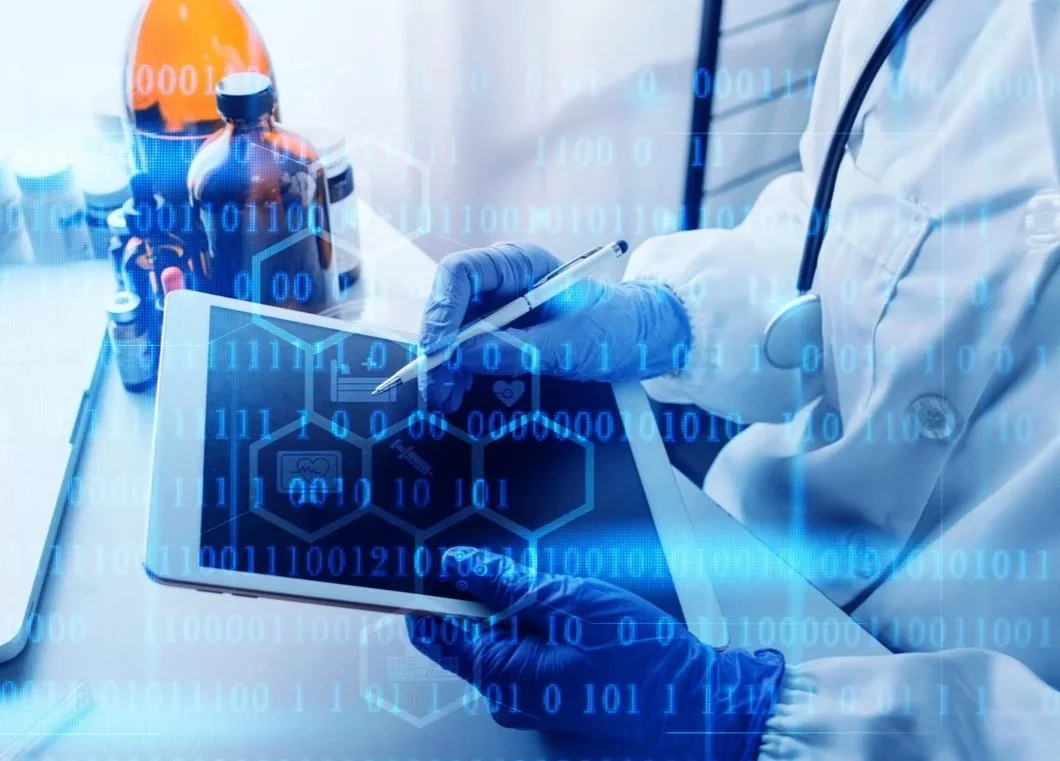 A healthcare professional in a lab coat and gloves uses a stylus to write on a tablet displaying medical icons, with medicine bottles and laboratory equipment in the background. Digital binary code overlays the image.