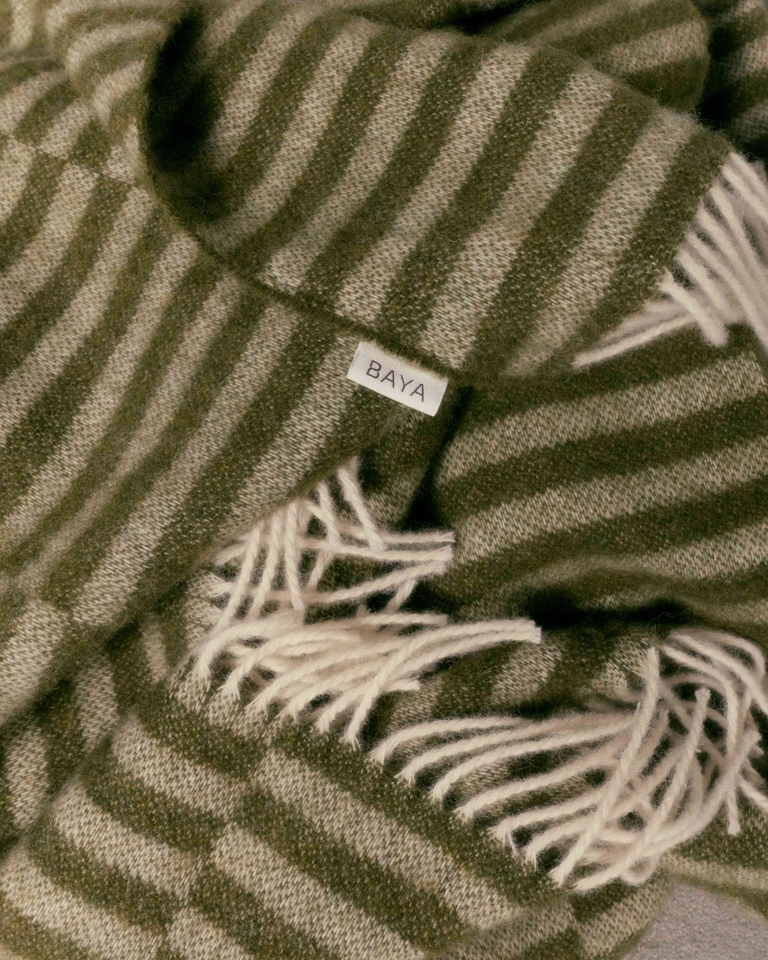 Close-up of a brown and beige striped scarf with fringed ends and a small white tag labeled 'BAYA'.