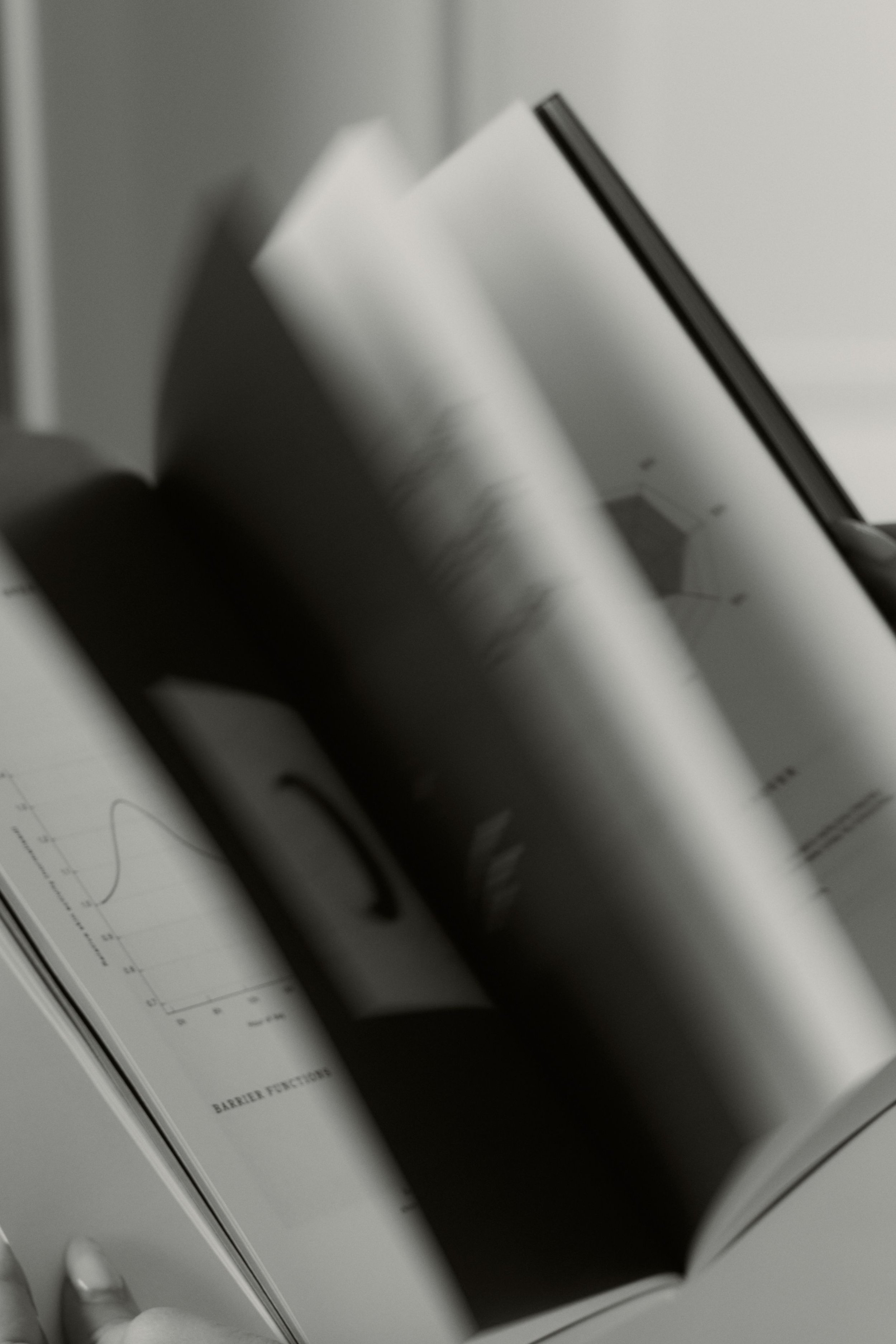 Open magazine with graphs and diagrams, in black and white, on a flat surface with a hand at the bottom left corner.