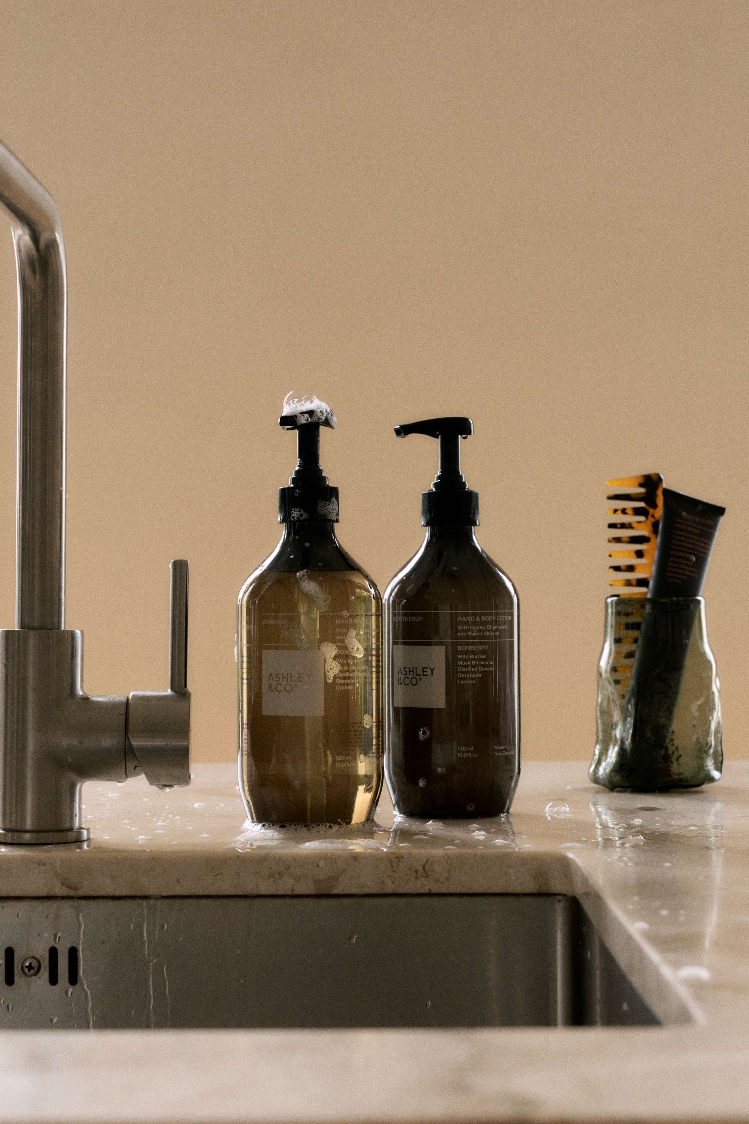 Bathroom sink with soap and lotion bottles labeled ASHLEY & CO, and a toothbrush holder with various toothbrushes.