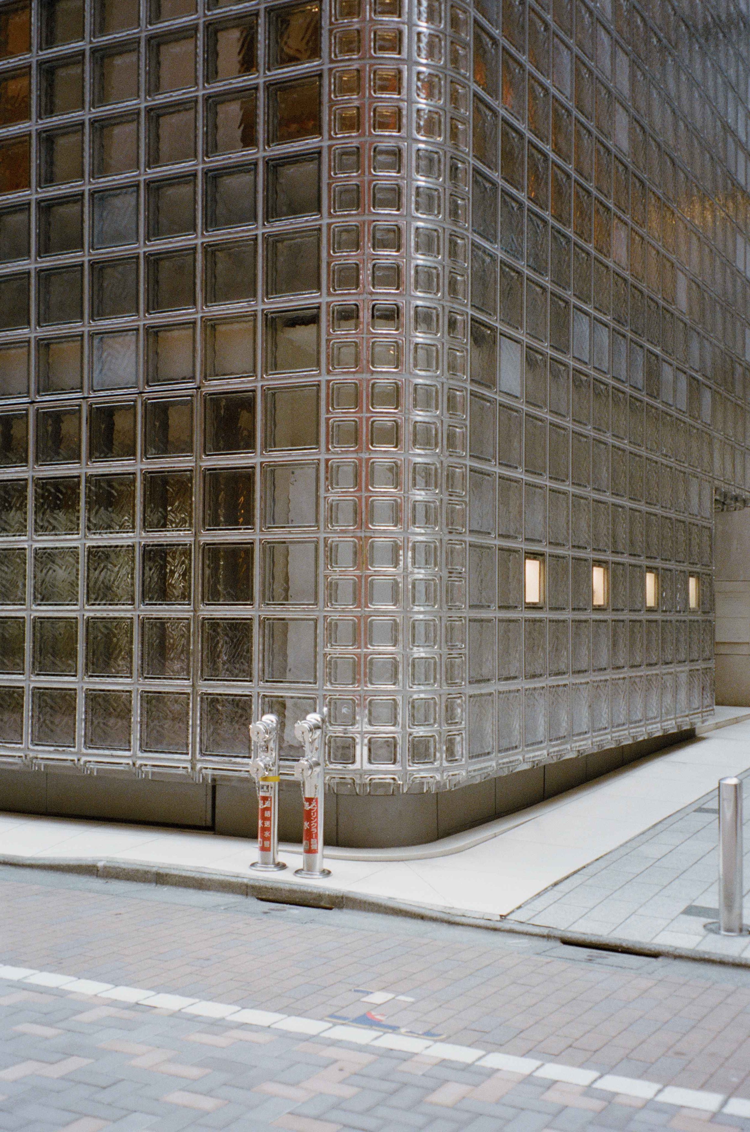 A building in Japan with a glass block wall and small rectangular windows, with two fire hydrants on the sidewalk.