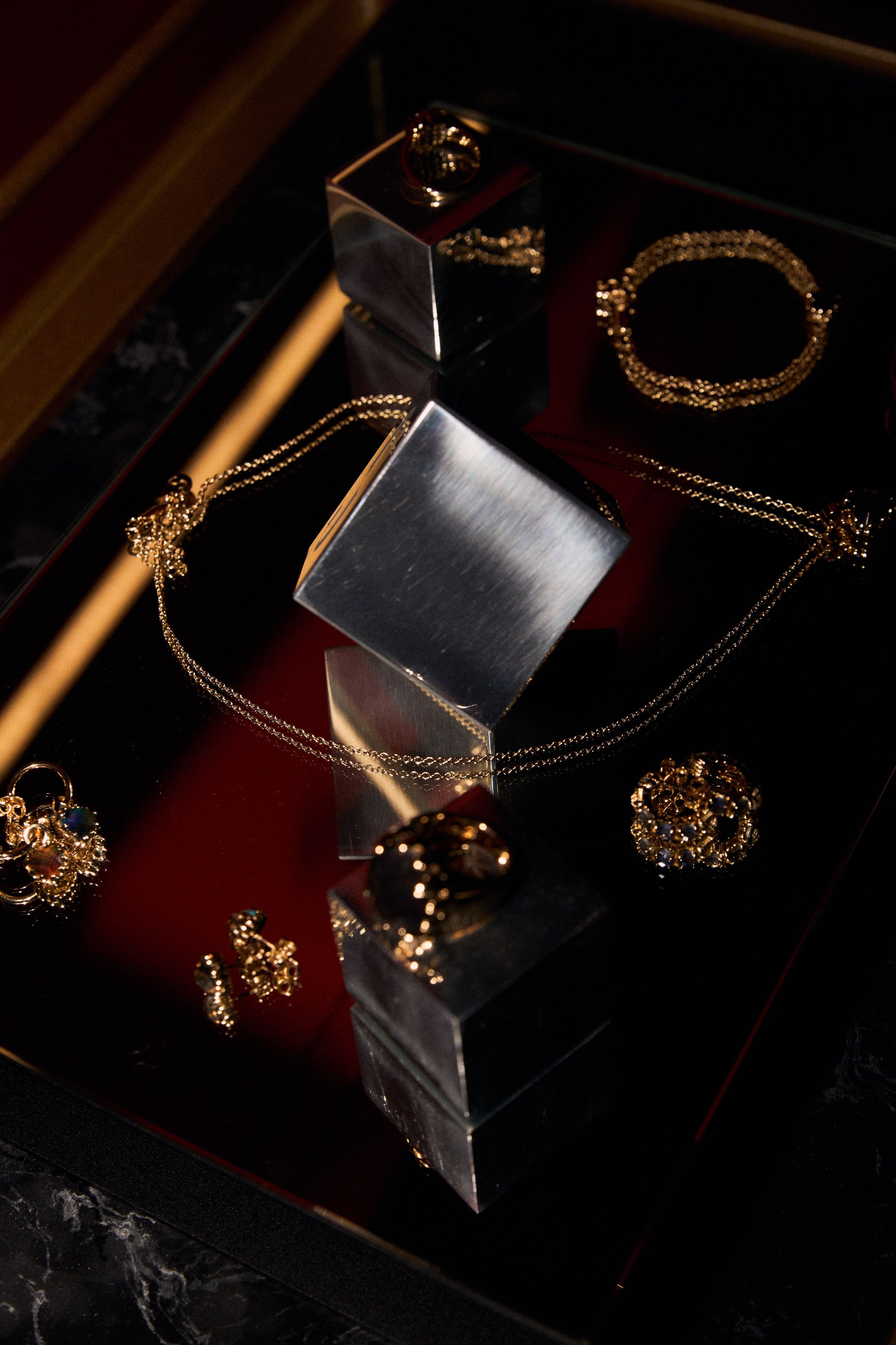 Gold Stolen Girlfriends Club jewelry displayed on black and red display stands, including necklaces, rings, and earrings.