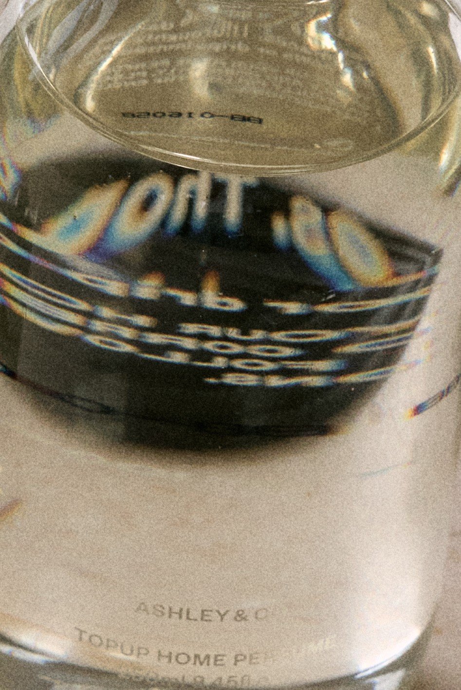 Close-up of a glass jar with a metal lid, reflecting a distorted and upside-down image of the surroundings, including the words 'Top Up' and part of the brand name 'Ashley & Co' on the label.