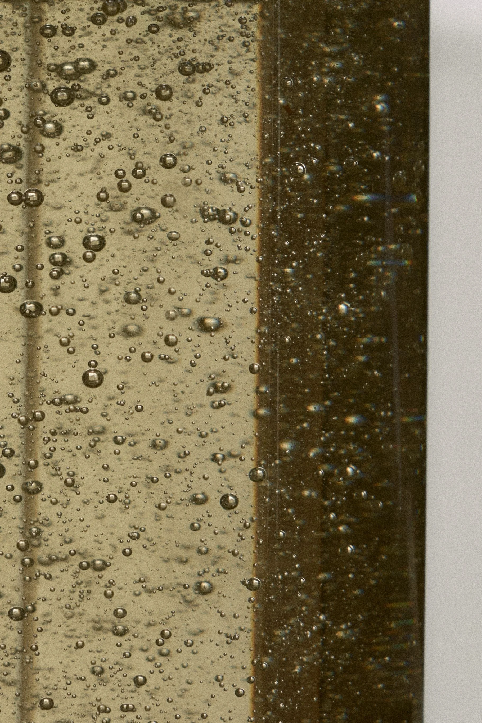 Close-up of a glass with bubbles in a dark liquid, Ashley & Co Soap, with a beige background.