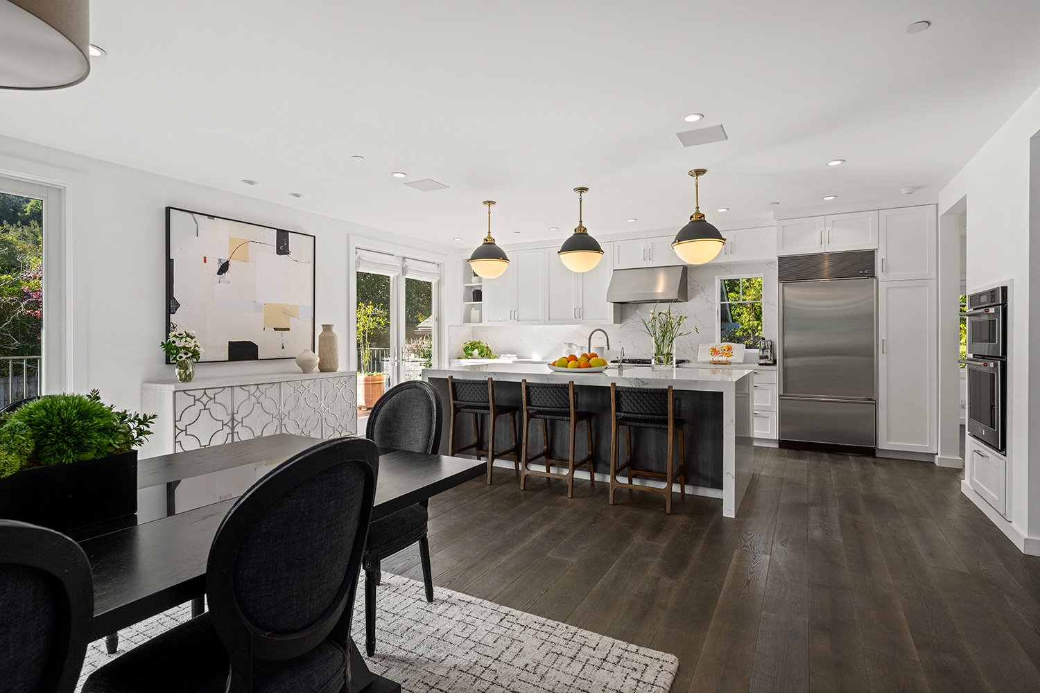 Modern kitchen with white cabinets, stainless steel appliances, dark wood floors, and a dining area with black chairs and a black table.
