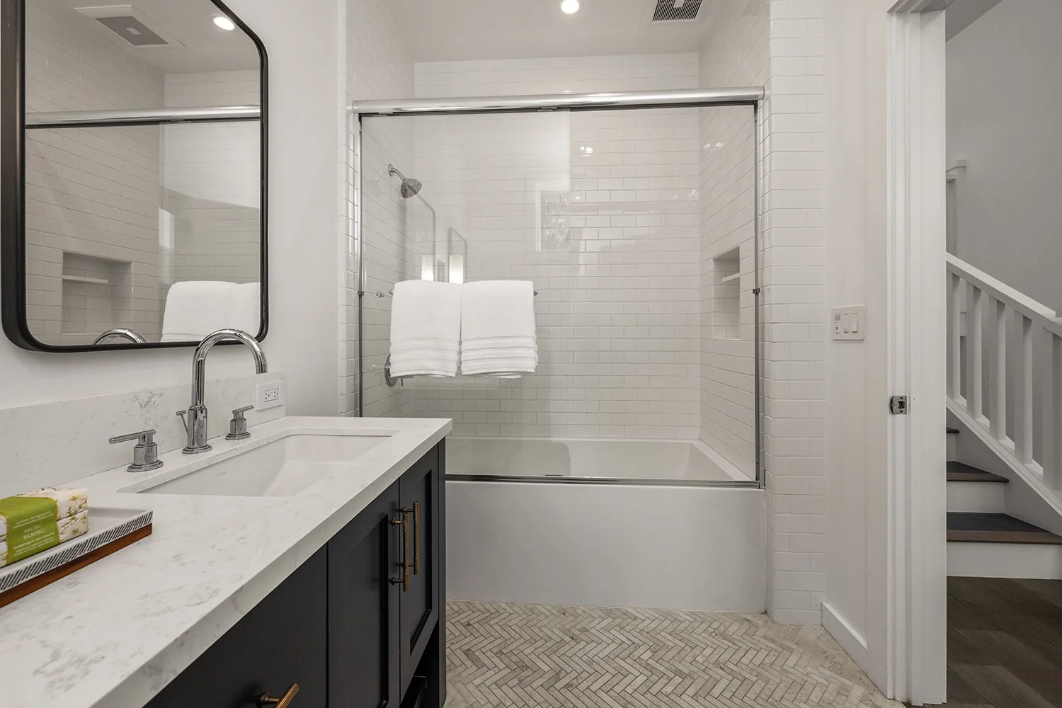 Modern bathroom with white subway tiles in the shower area, a black vanity with a white marble countertop, a mirror, and two neatly folded white towels hanging on a towel bar.
