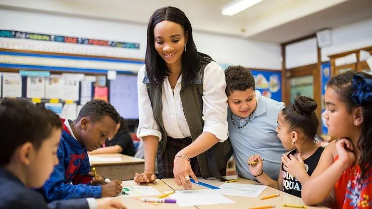 Une enseignante souriante avec des élèves d'école primaire assis autour d'une table en classe
