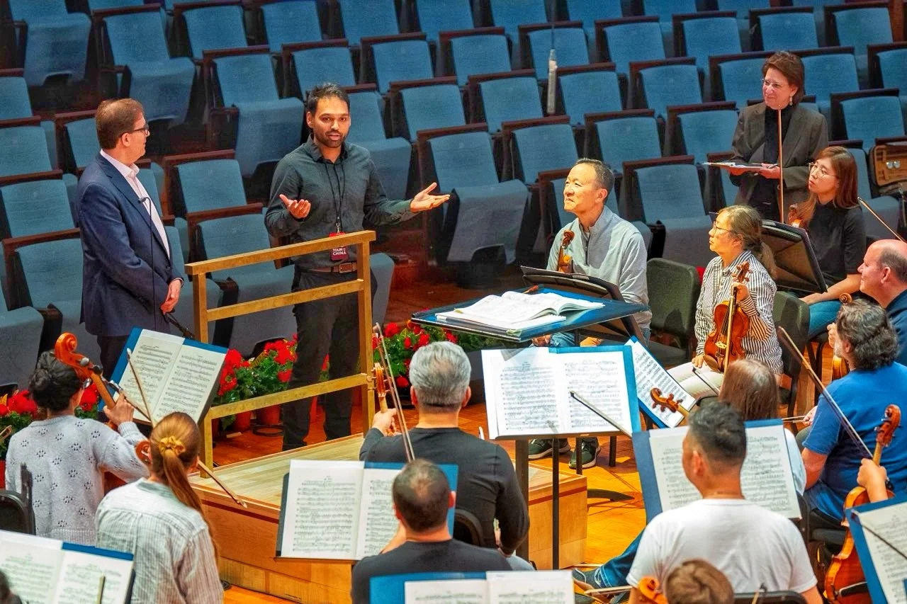 Conductor and orchestra during rehearsal in concert hall with empty seats.