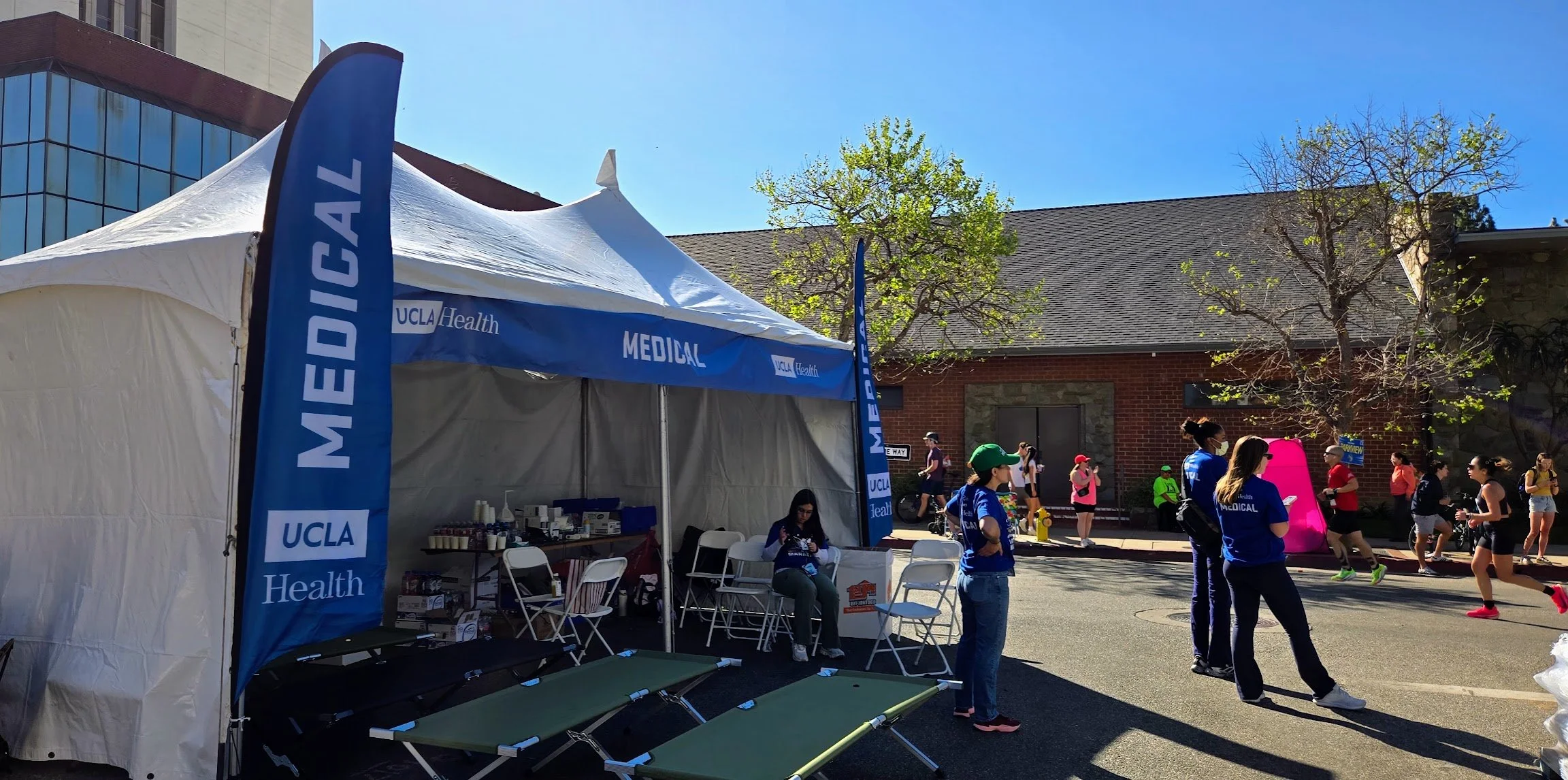 UCLA Health medical tent at a running event, with people gathered around and runners passing by on the street.