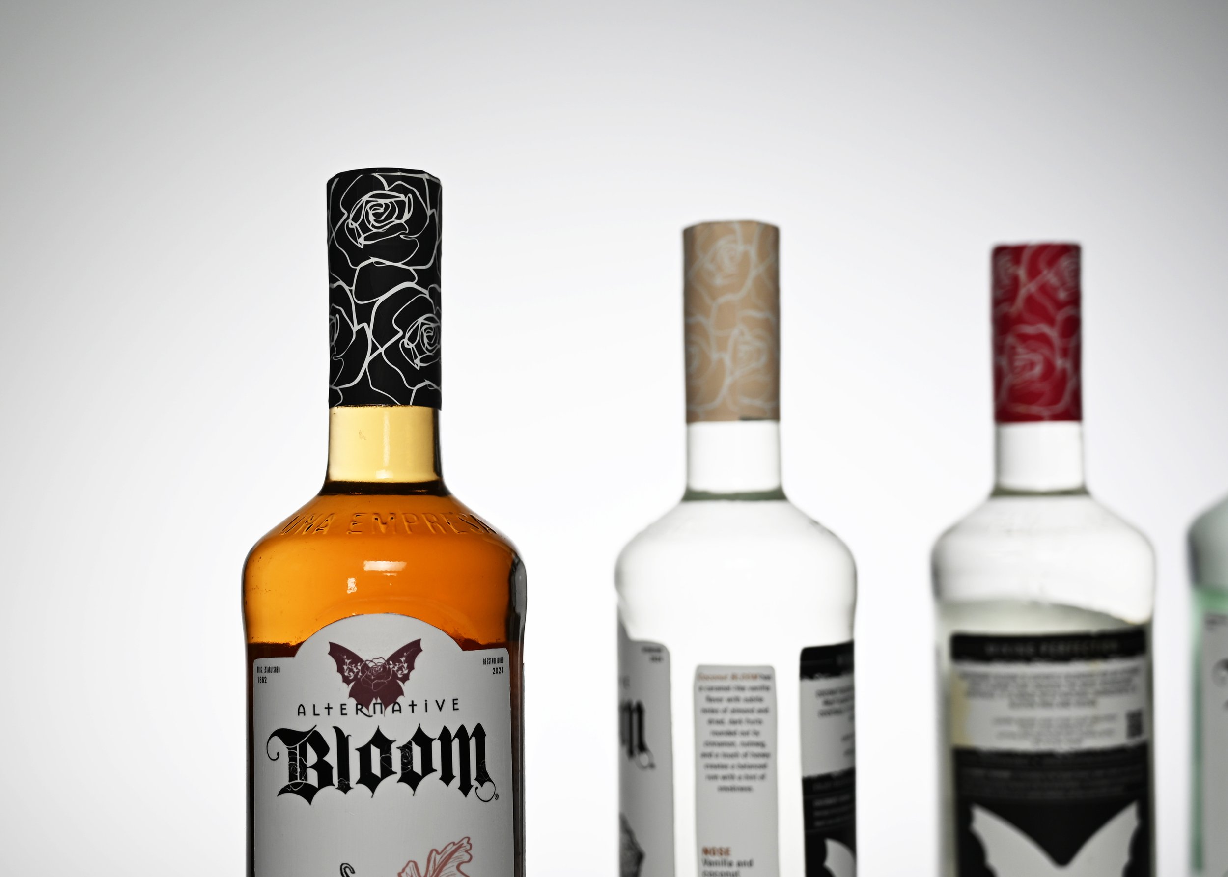 Close-up of four bottles with different decorative caps, including black with white line art of roses, beige with similar floral design, and red with floral pattern, on a white background.