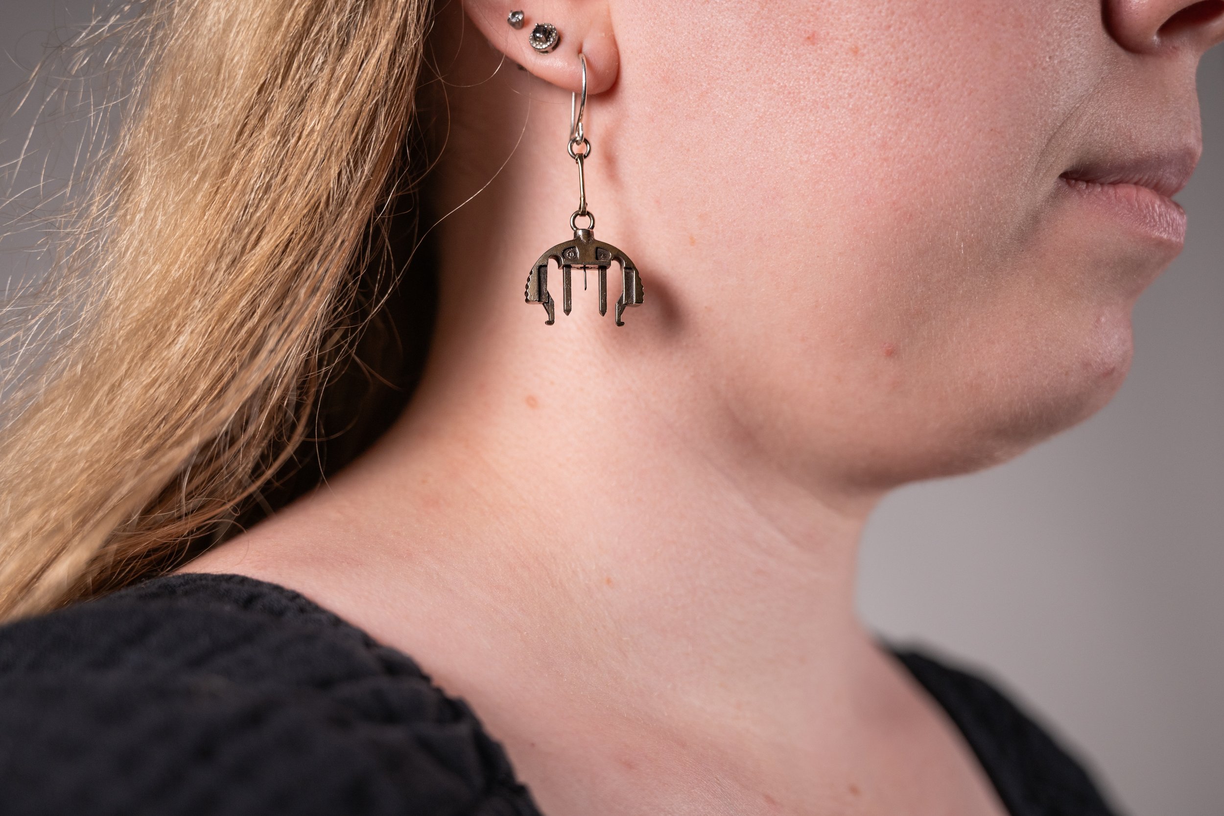 Close-up of a woman's face, showing her ear with multiple earrings, including a large earring featuring a infusion set design.