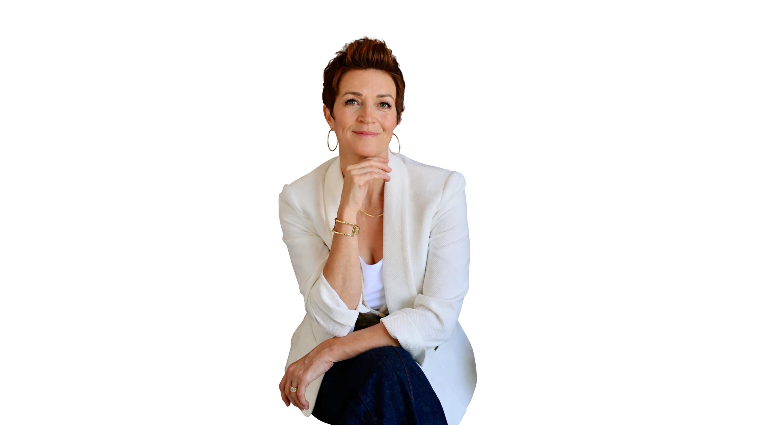 A woman with short brown hair wearing a white blazer, white shirt, and jeans, sitting with her hand resting on her chin, smiling slightly against a black background.